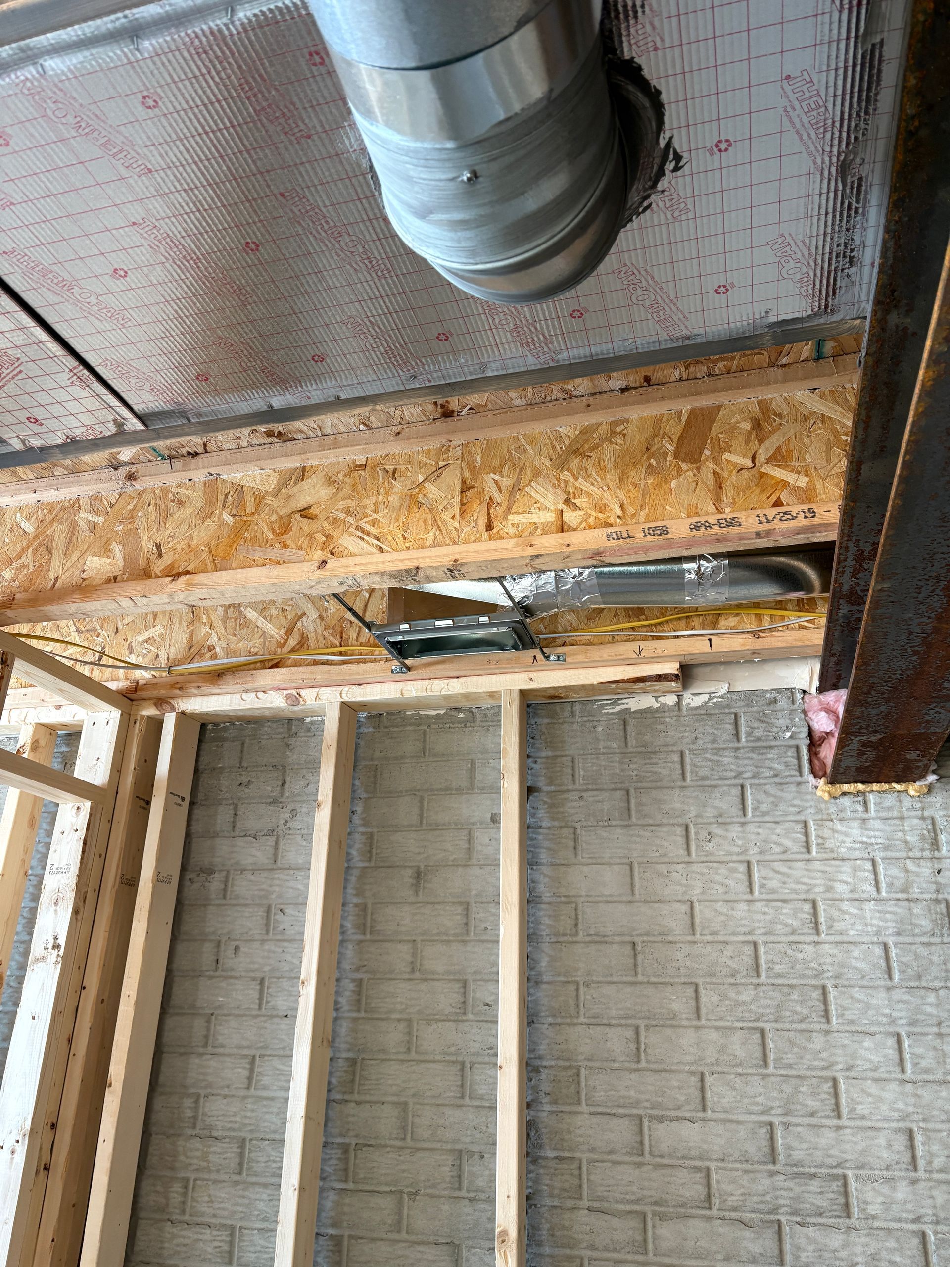 Interior view of exposed construction. Ventilation ducting, wood framing, brick wall.