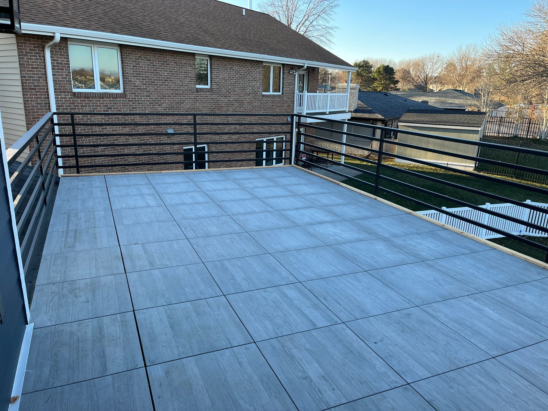 A newly built wooden deck with a black railing, connected to a brick house. The deck is a light gray color.