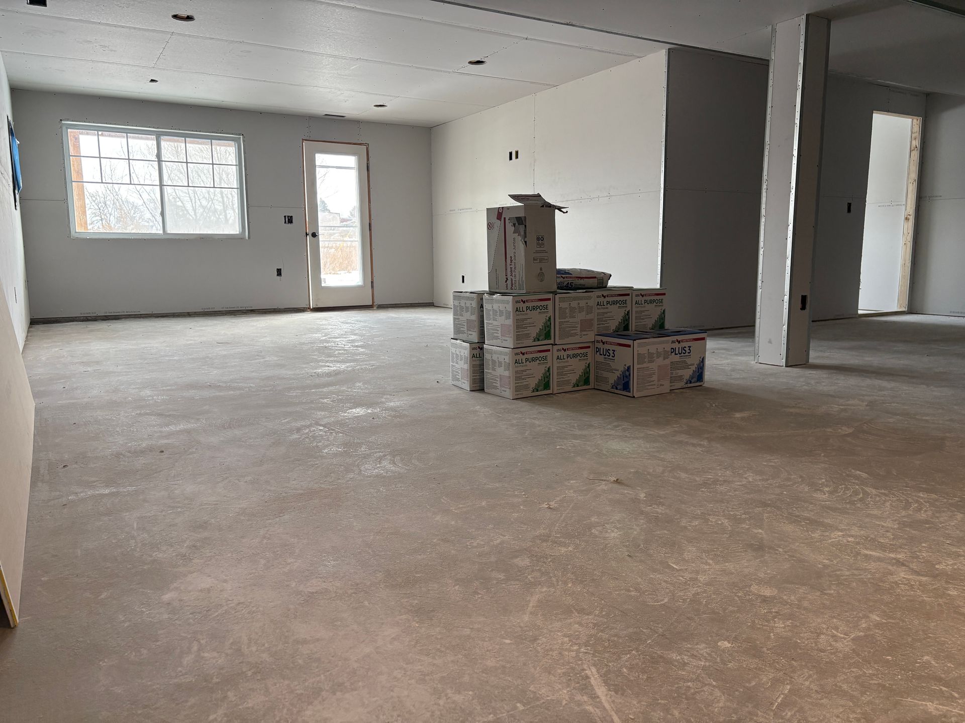 Empty room under construction with stacked boxes and a window and door.