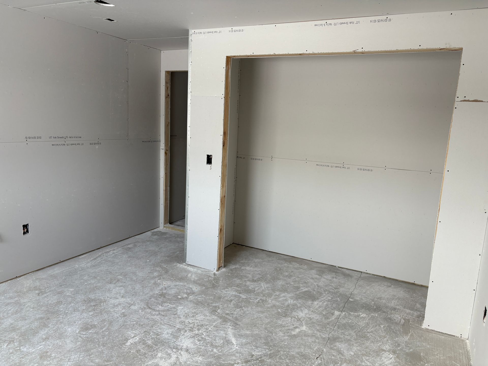 Empty room under construction, drywall walls, unfinished doorway, concrete floor.