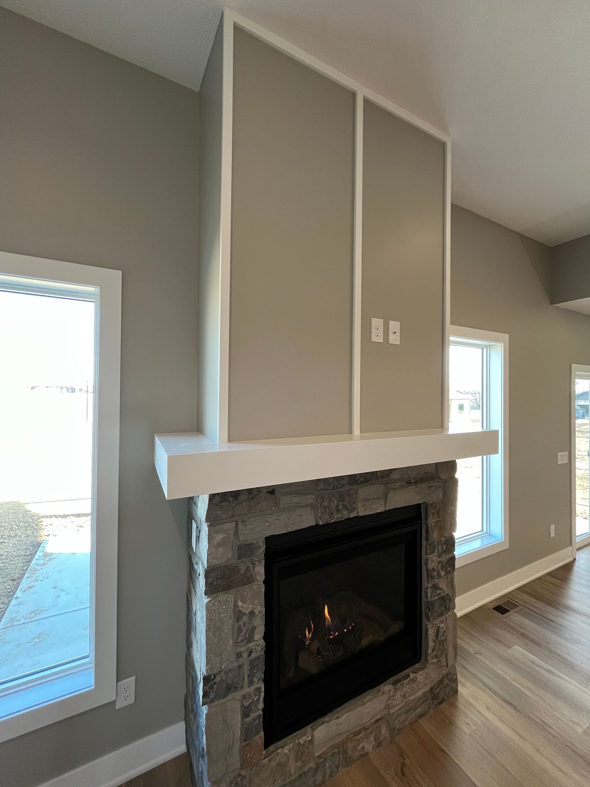 An open living space with a linear fireplace on a white wall, a floating wood mantel with lighting beneath, wood-look flooring and a gold chandelier.