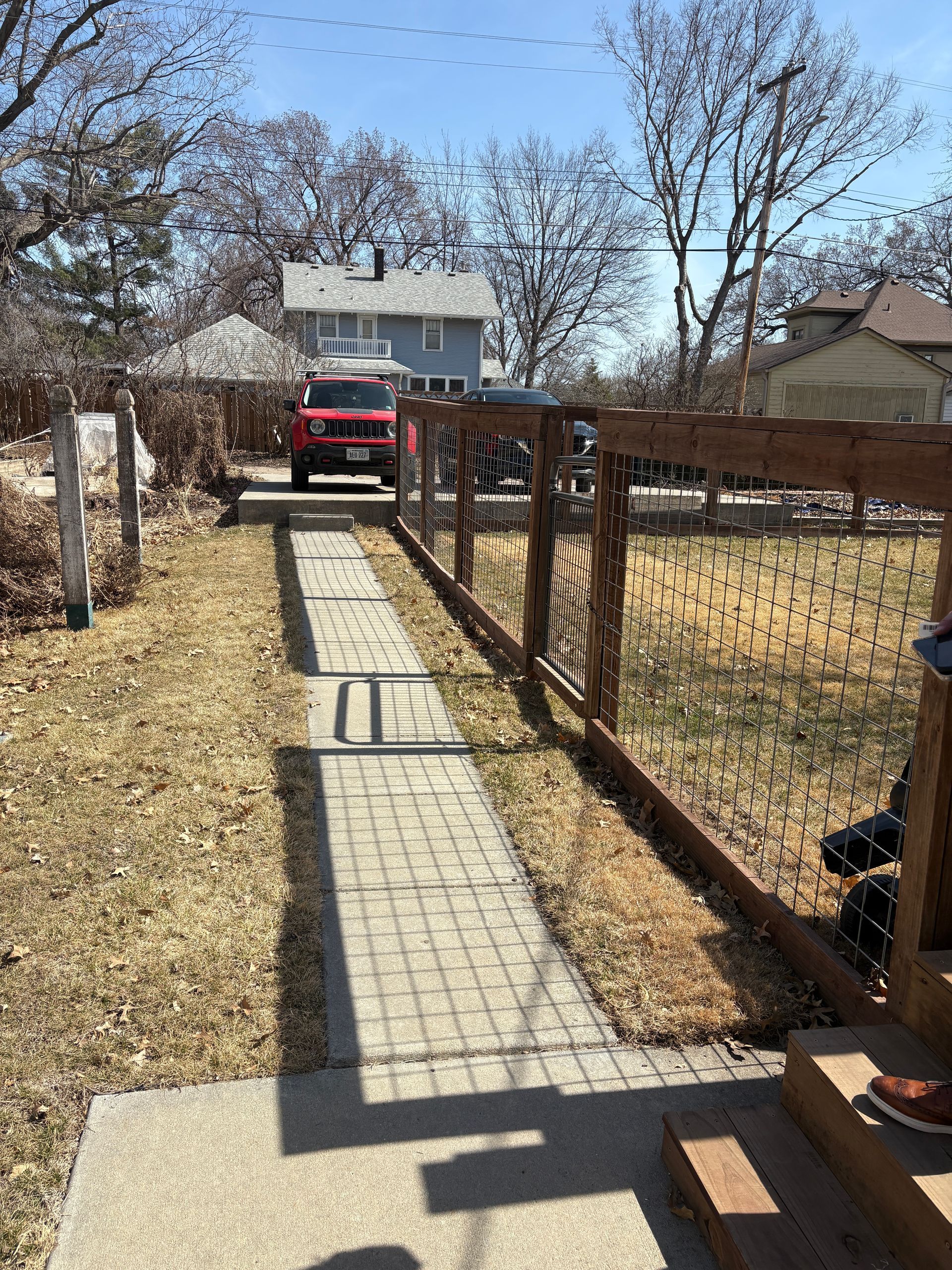 A brick path leads to a red truck parked in front of a light blue house; fenced yard with dried grass.