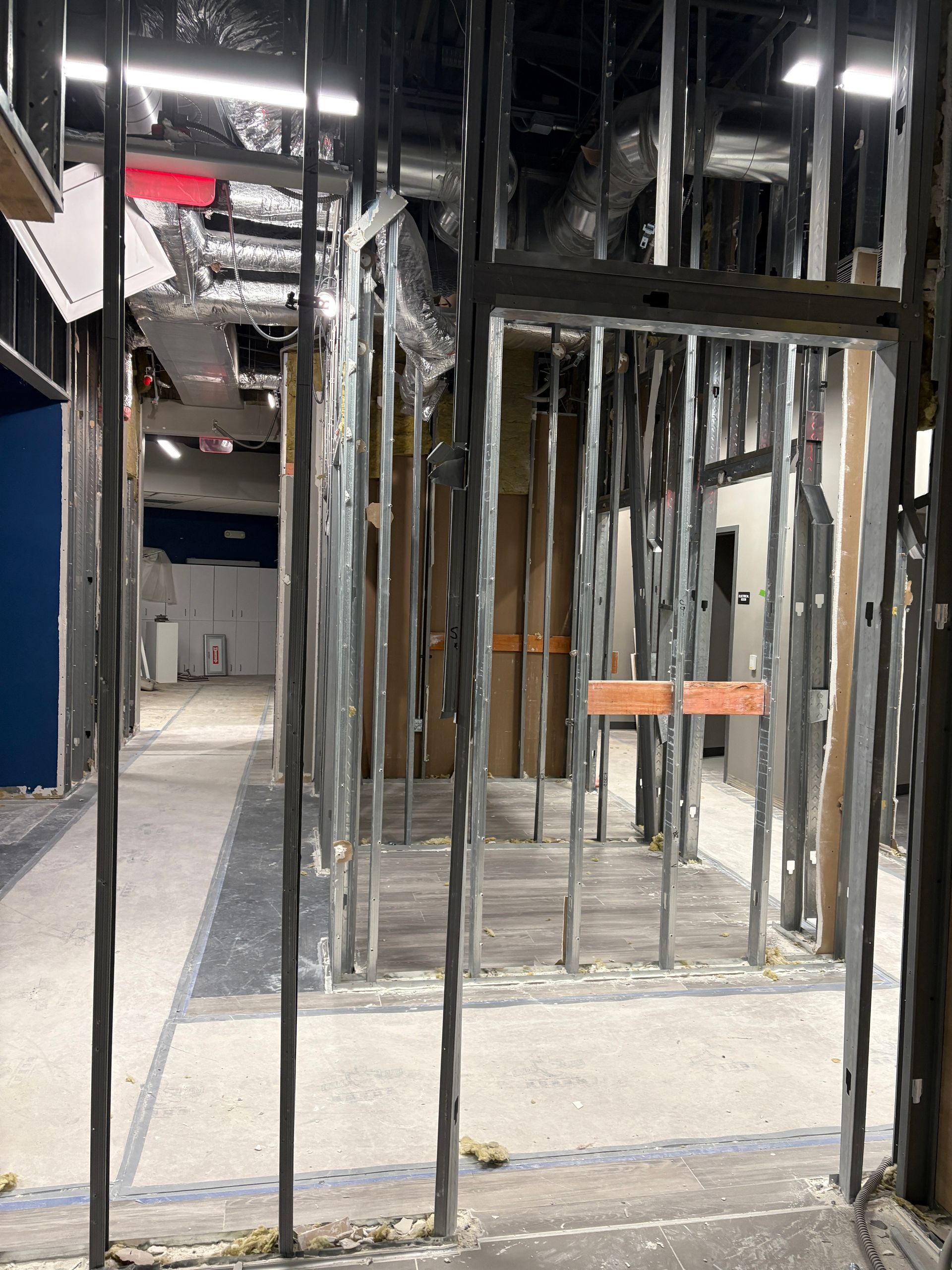 Interior view of a building under construction, showing metal framing, open doorways, and exposed utilities.