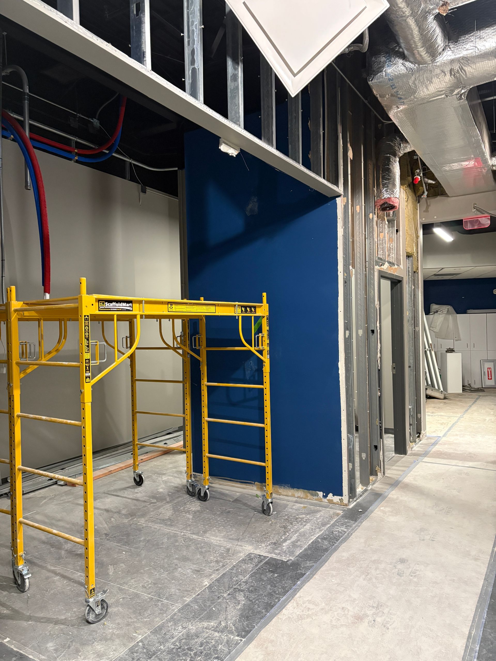 Construction site: yellow scaffold, blue wall, metal framing, unfinished hallway.