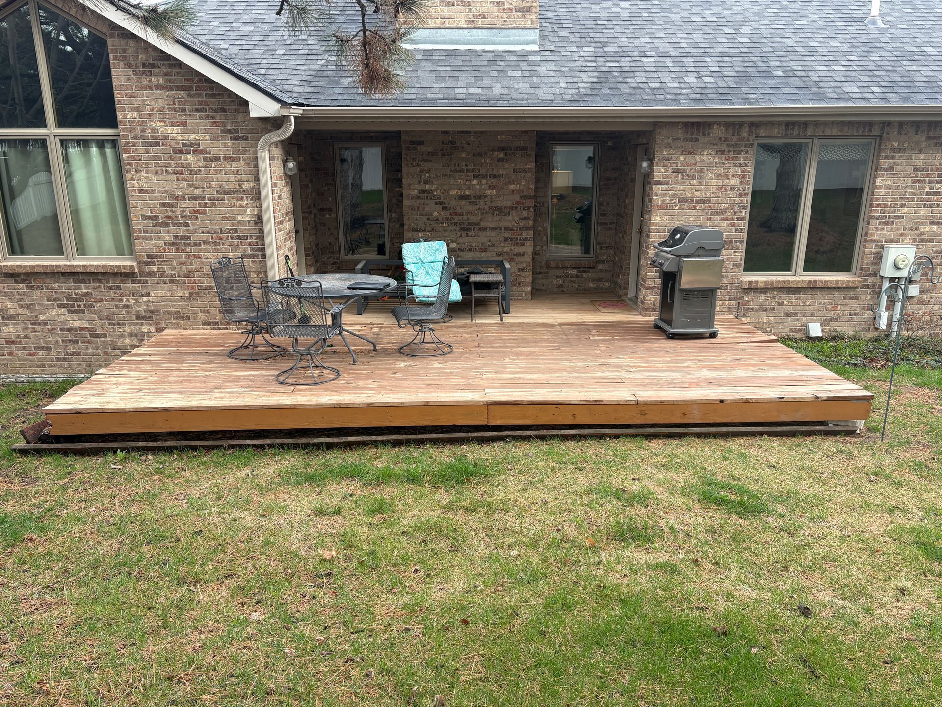 Wooden deck with patio furniture, grill, and a brick house in the background.
