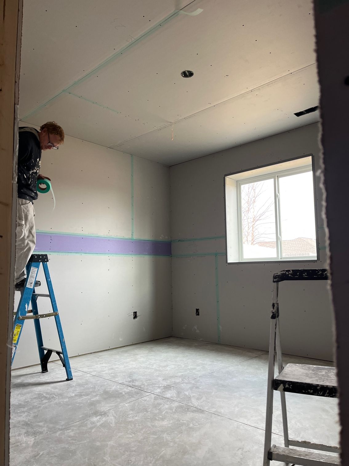 A man is measuring the ceiling of a room with a tape measure.