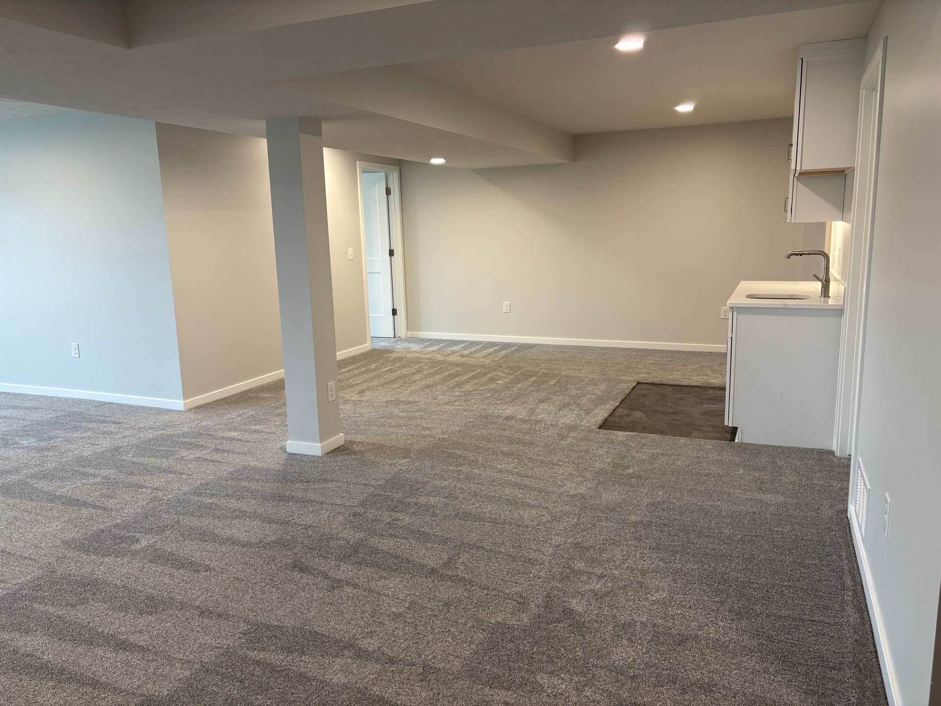 Finished basement with gray carpet, neutral walls, a small sink, and recessed lighting.