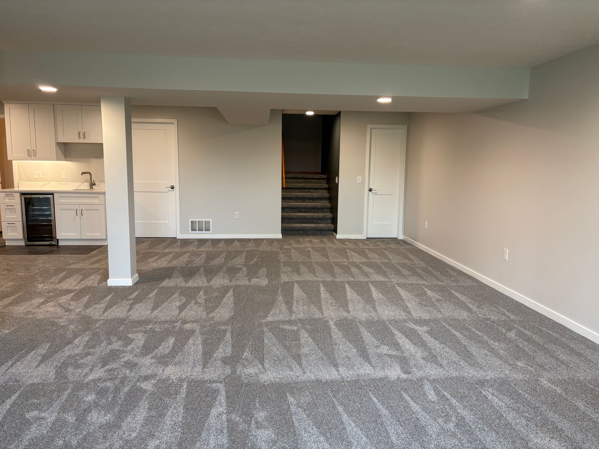 Basement room with gray carpet, white cabinets, and a staircase leading up.