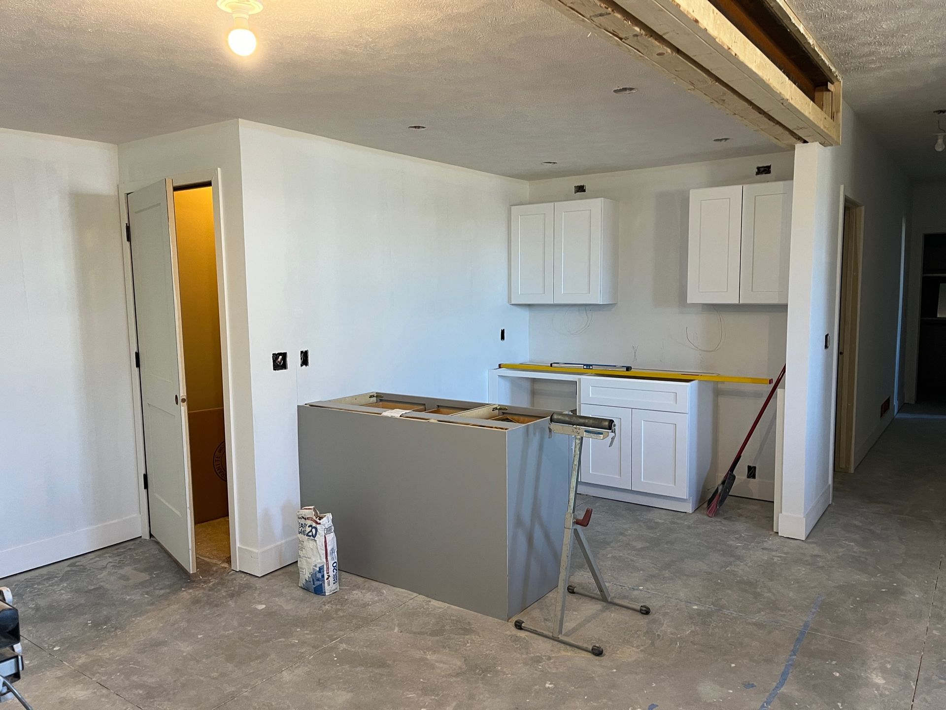 A kitchen under construction with white cabinets and a gray island