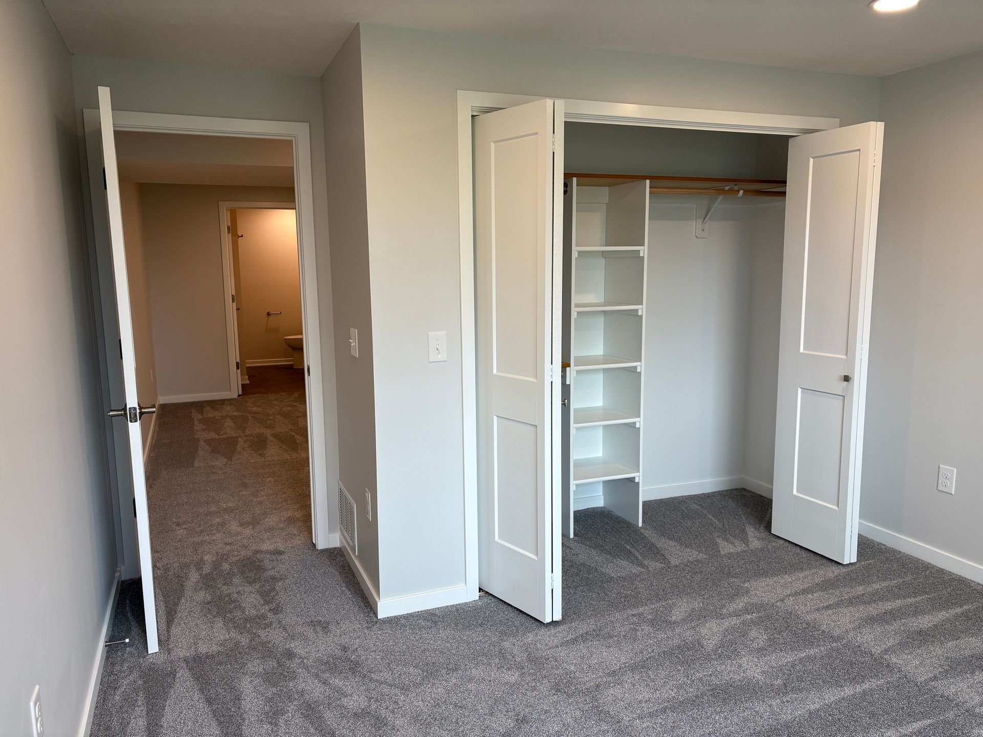 Bedroom with gray carpet, closet with shelves, and open door to a hallway.
