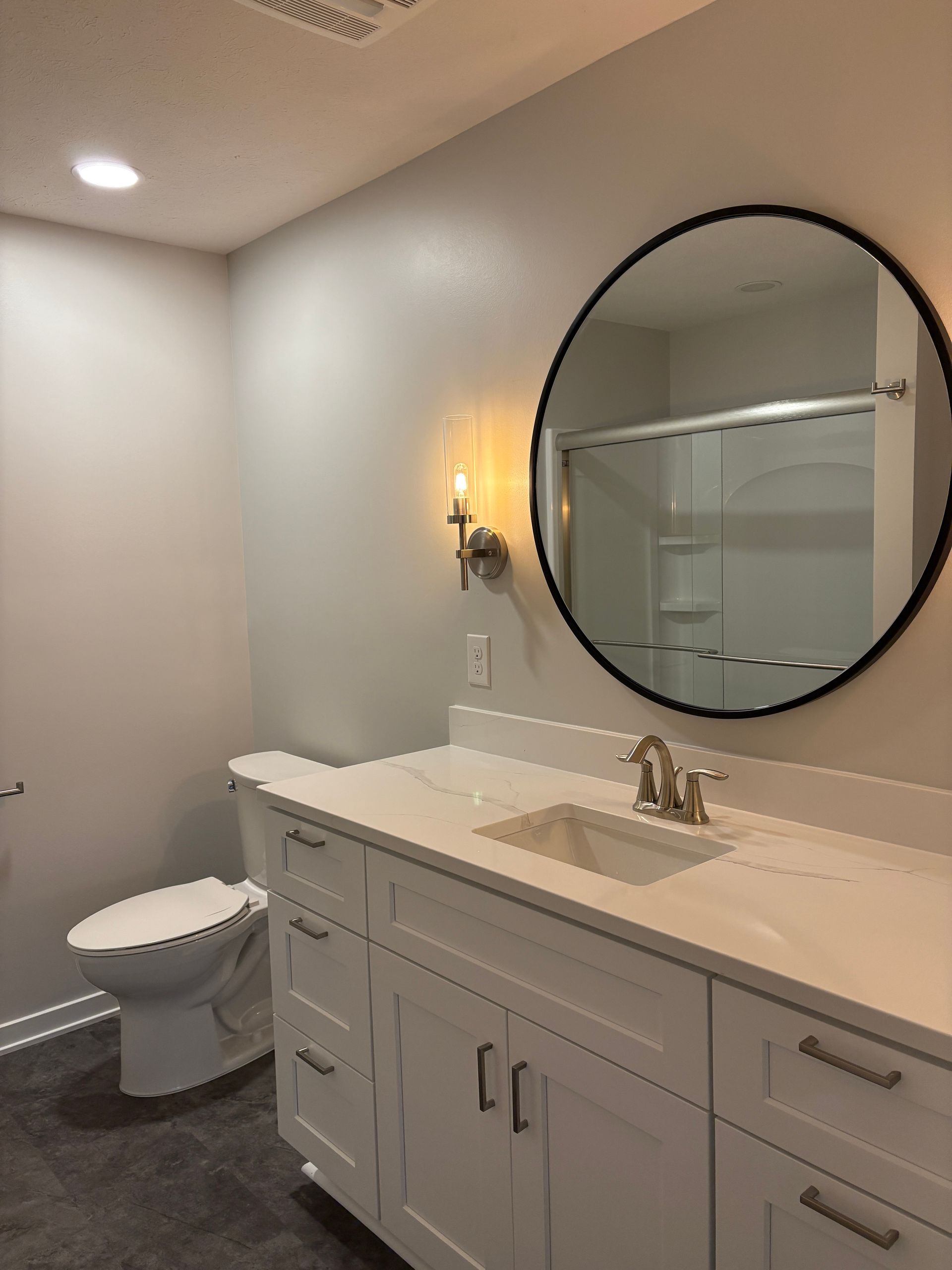 Bathroom with white vanity, toilet, and a round black mirror.