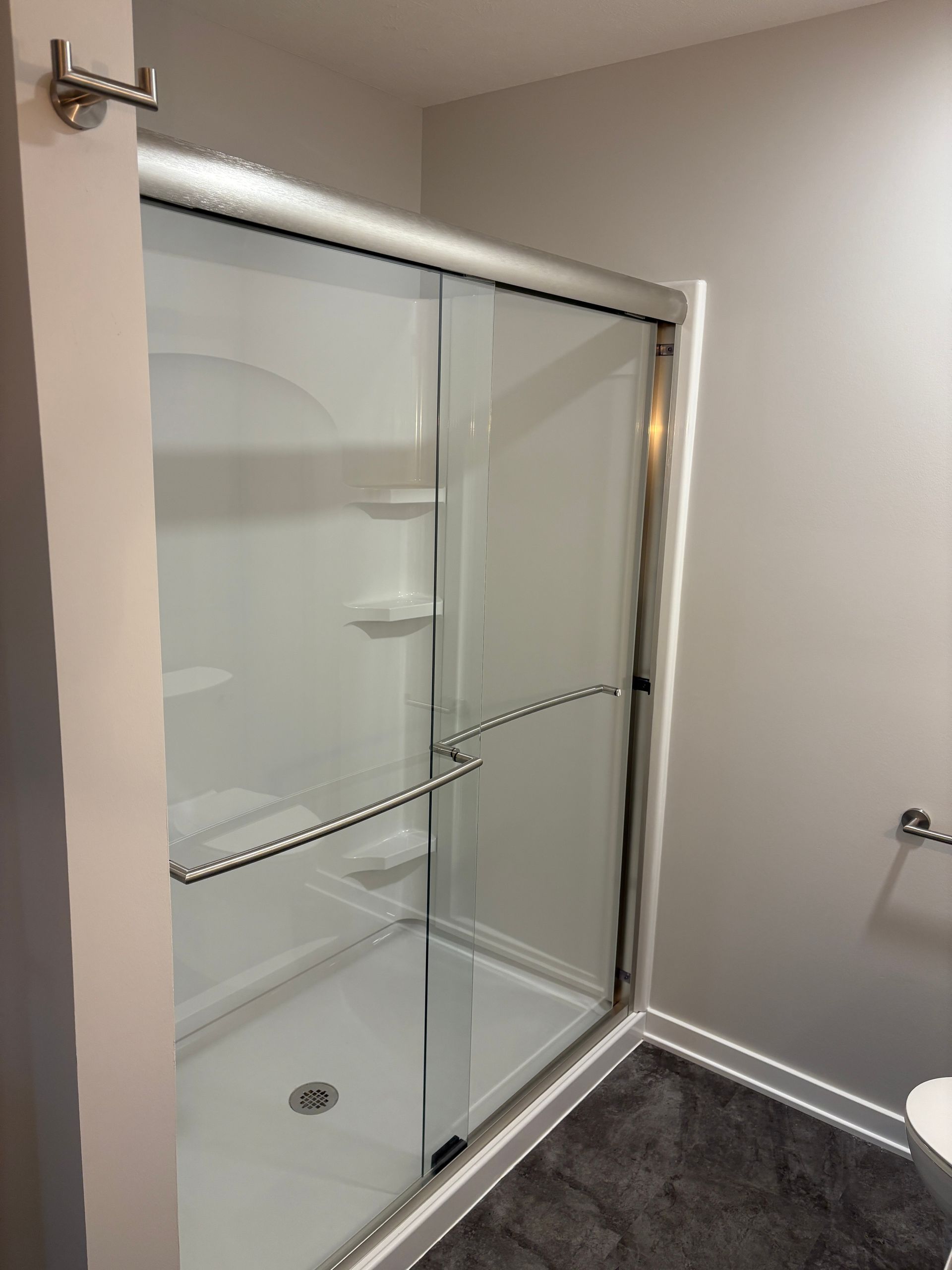 White shower stall with sliding glass doors in a bathroom; gray walls and dark gray rug.