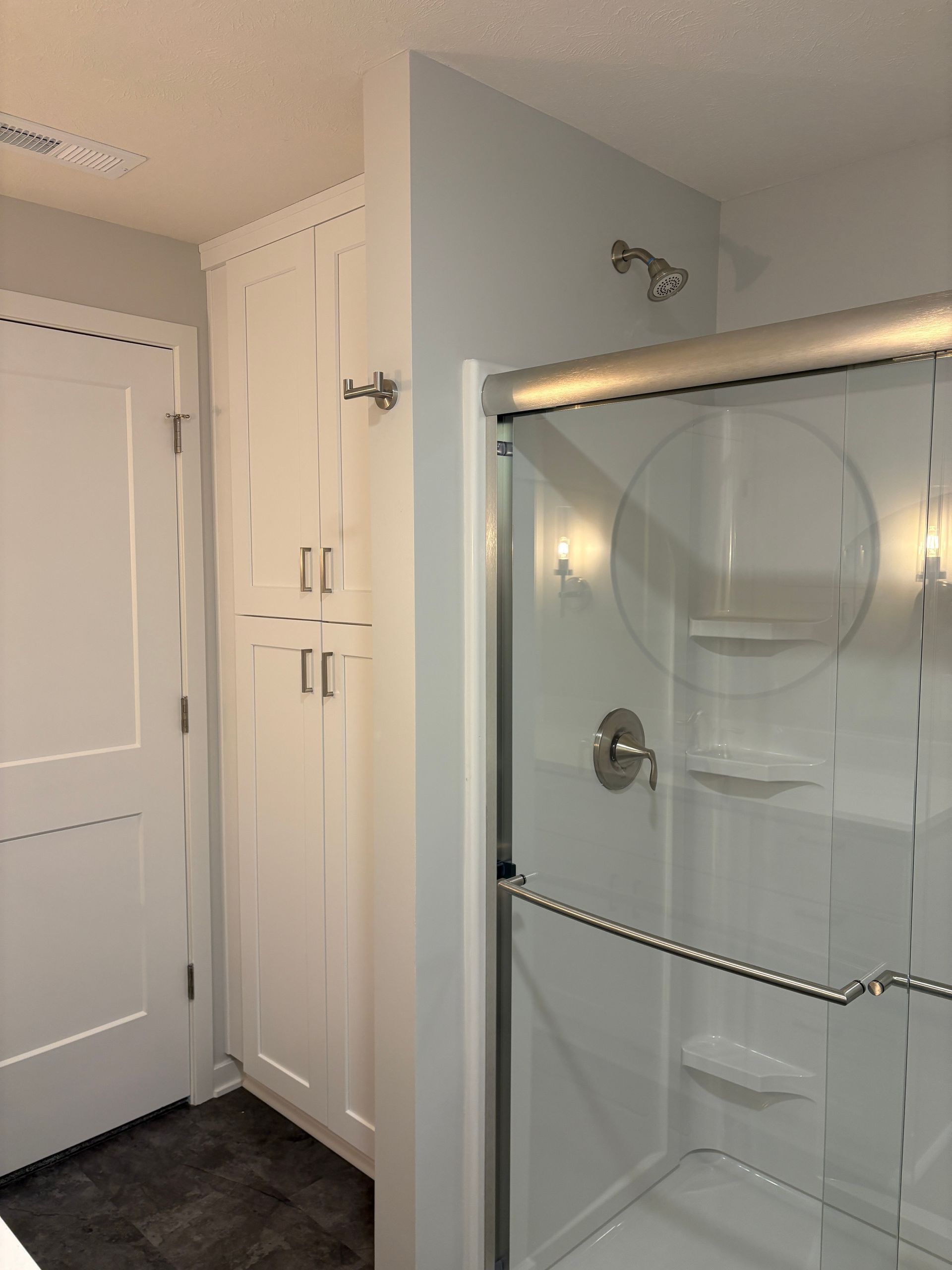 White bathroom with a shower, tall storage cabinet, and door; light blue walls.