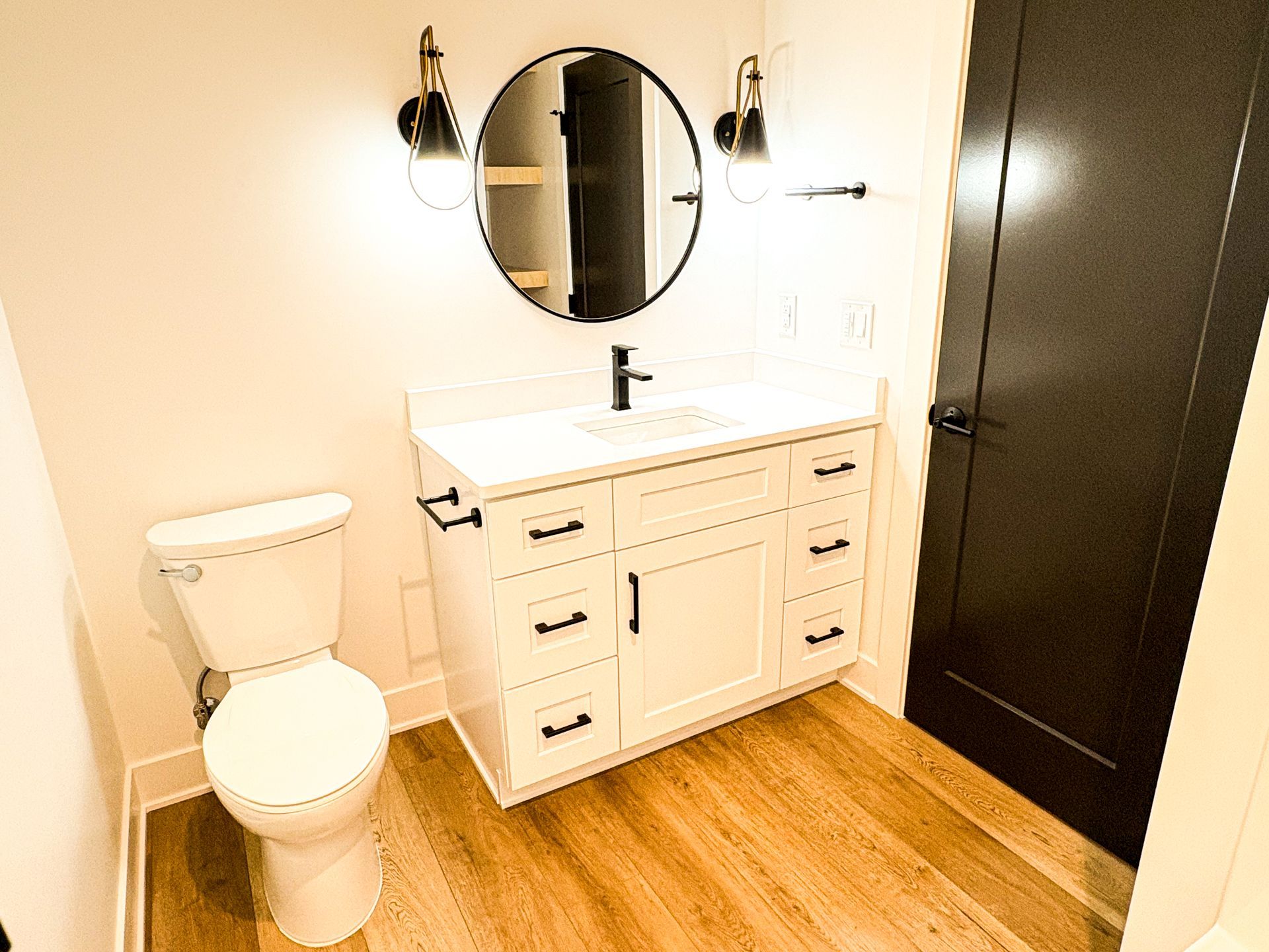 Bathroom with white vanity, black hardware, round mirror, and black door.