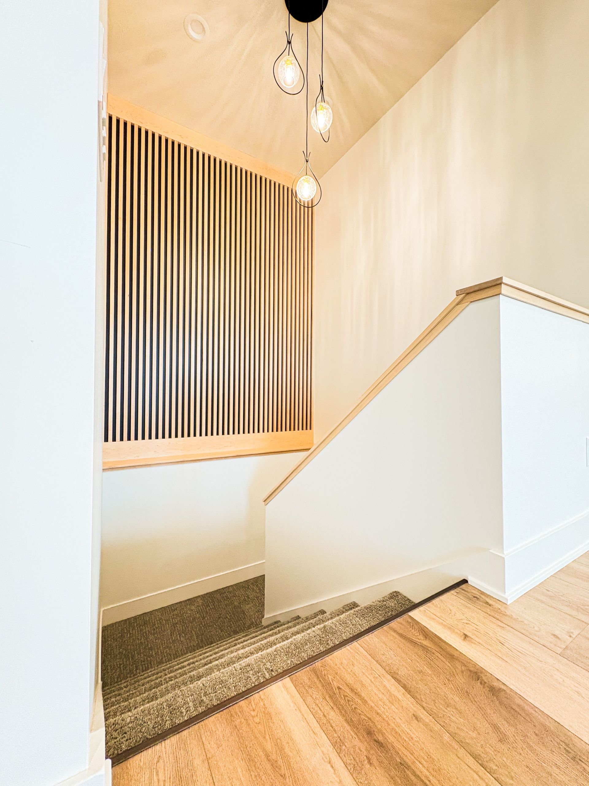 Staircase with wooden floor and railing, textured wall panel, and pendant lights.