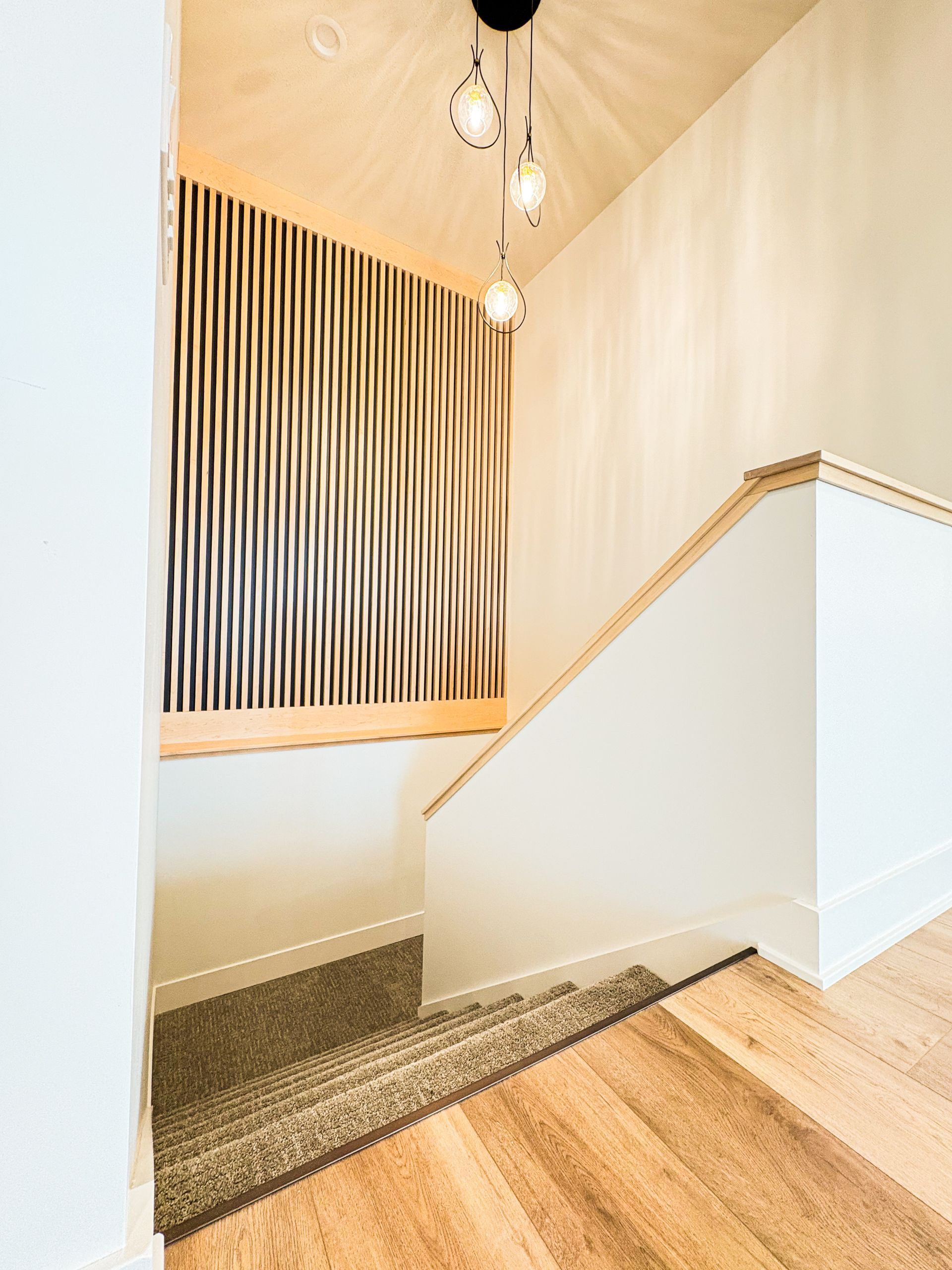 Stairwell with wood floor, carpeted steps, textured accent wall, and hanging lights.