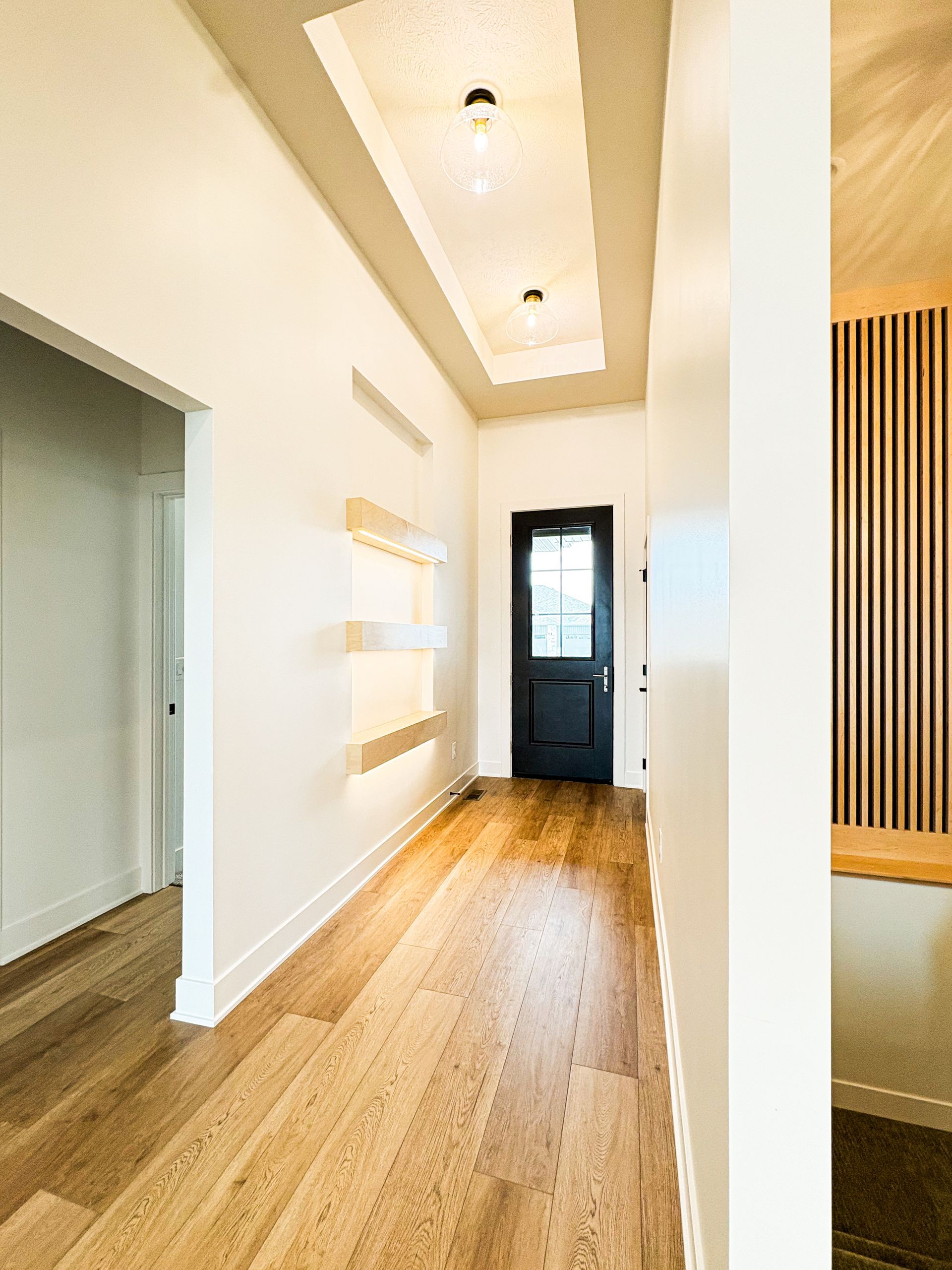 Hallway with wood floors, recessed ceiling with lights, and black door.