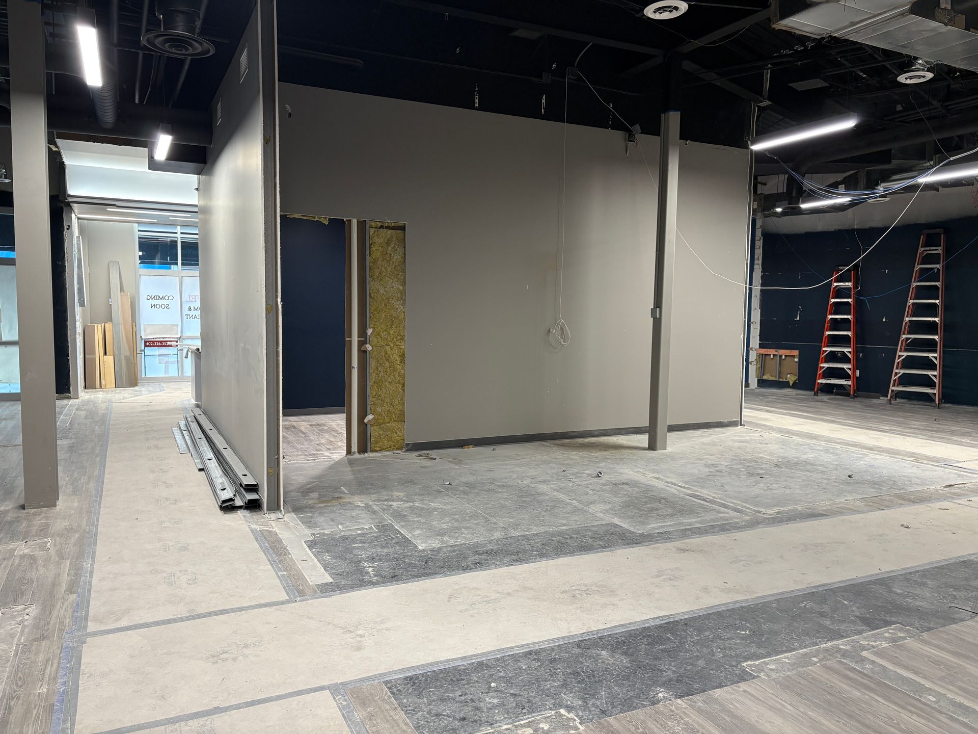 Interior of a construction site: walls partially built, concrete floor, two ladders, and a doorway.