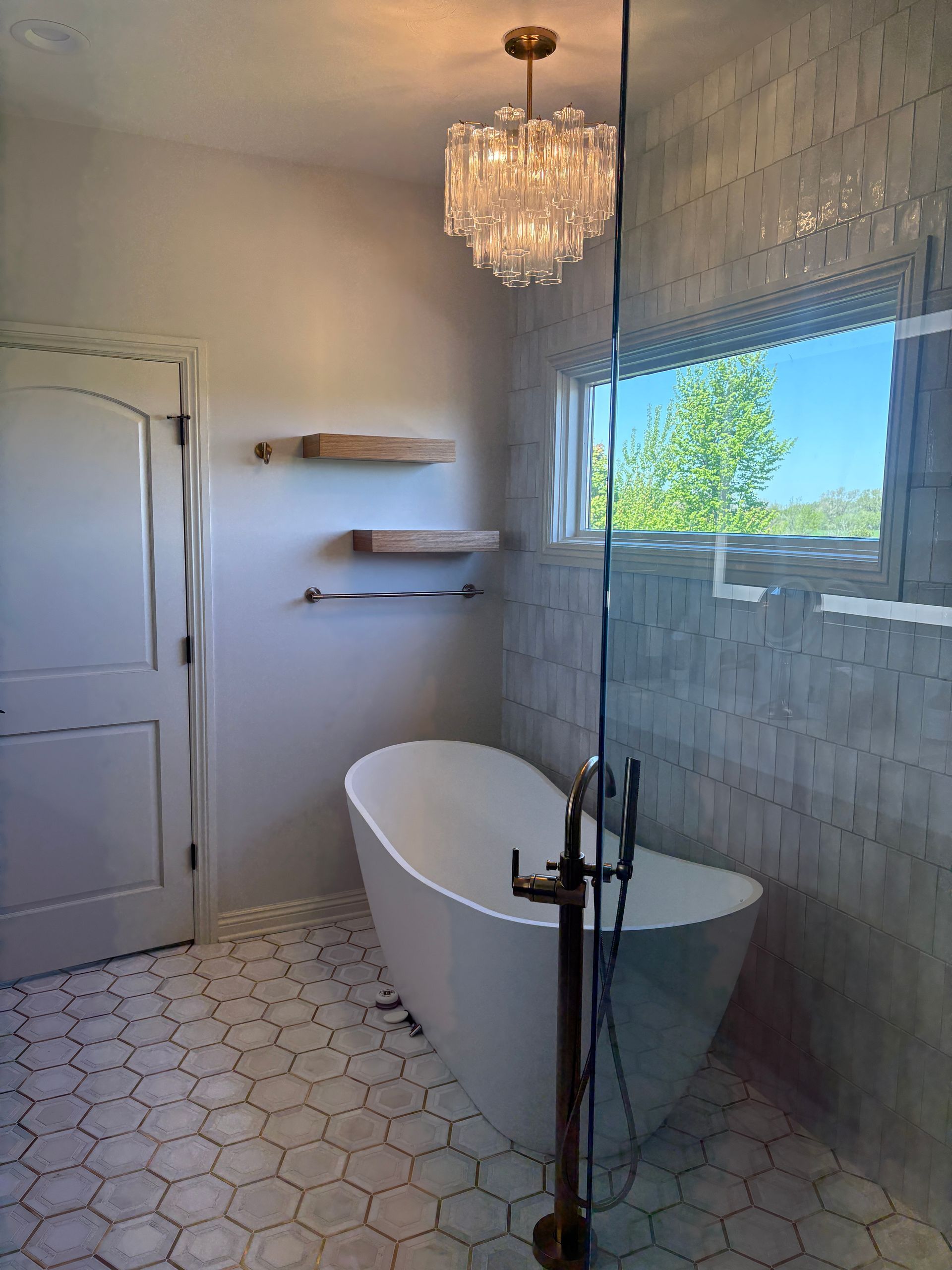 Bathroom with a freestanding tub, hexagon tile floor, and a chandelier.