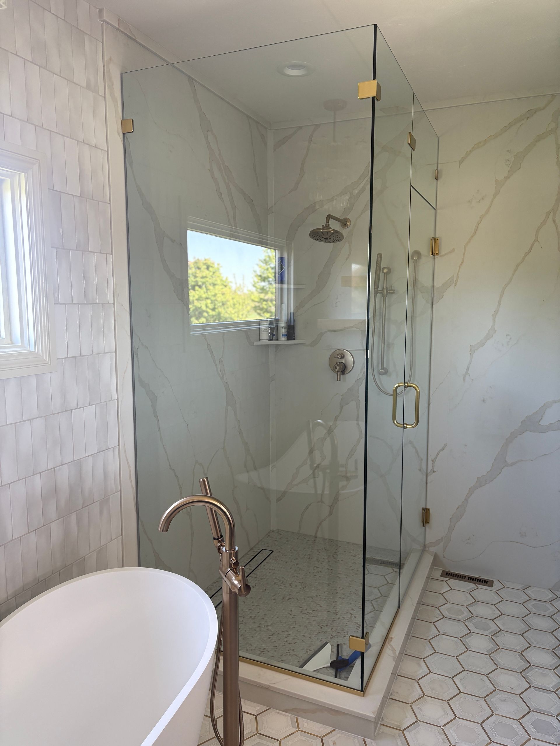 Luxurious bathroom with glass shower and freestanding tub, white marble walls, gold fixtures.