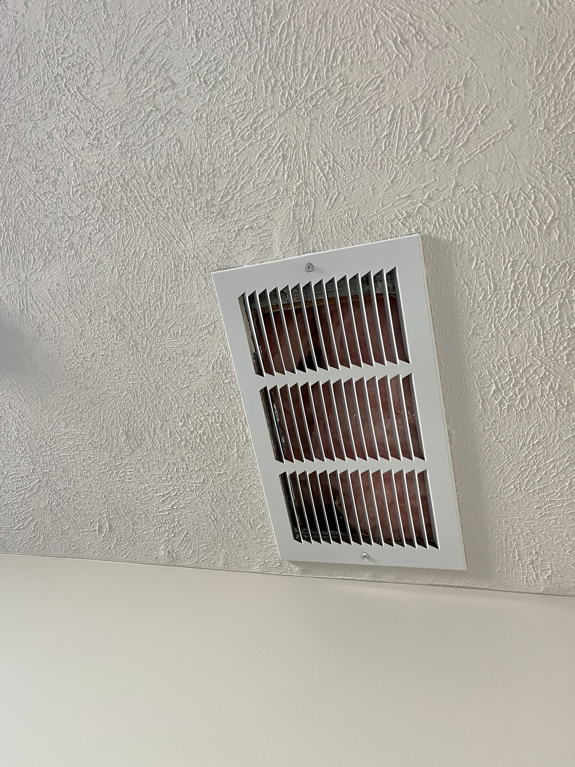 A white air vent is hanging from the ceiling of a room.