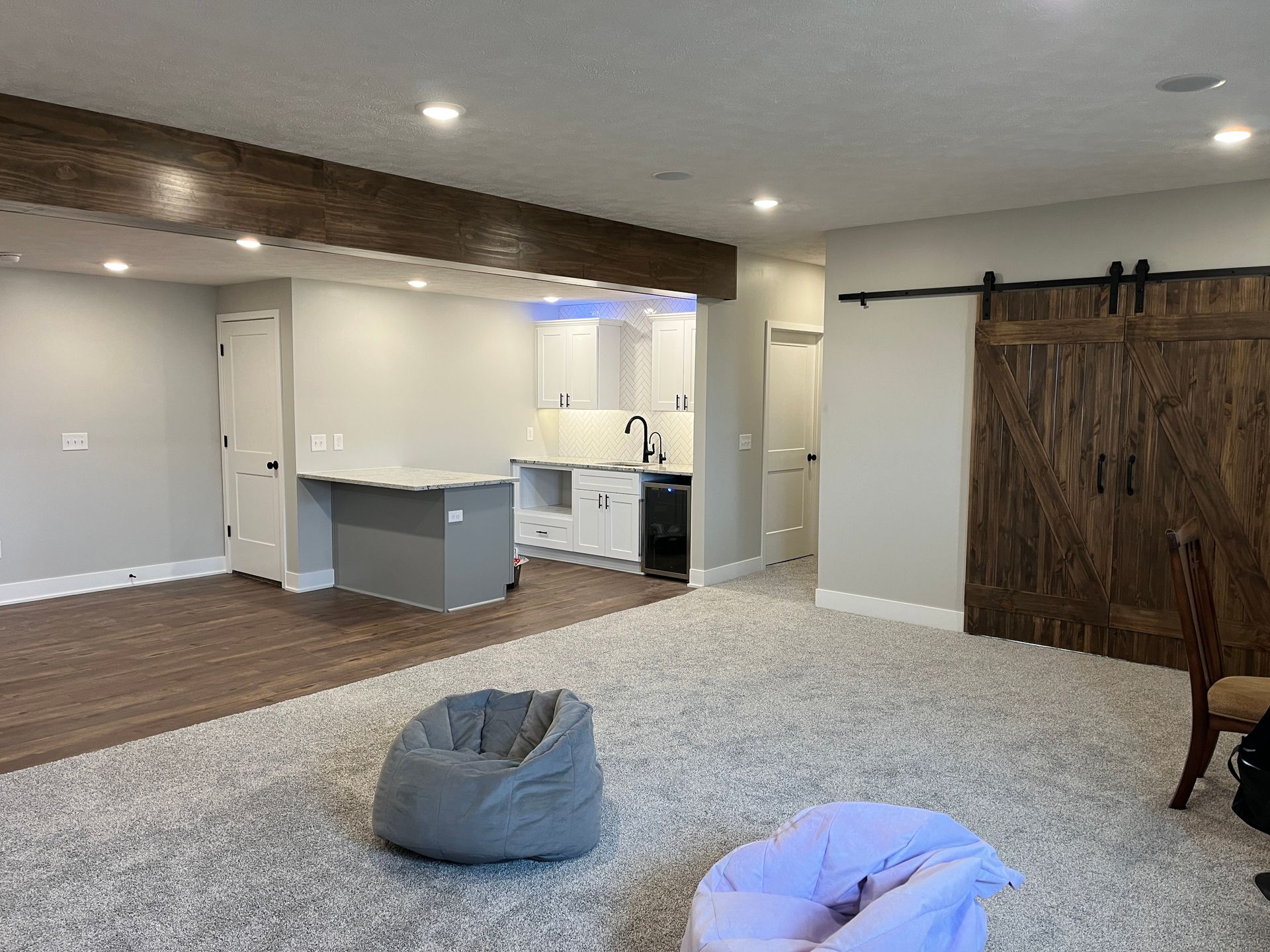Cozy finished basement with kitchen, wood accents, and barn door; two beanbag chairs on a light carpet.