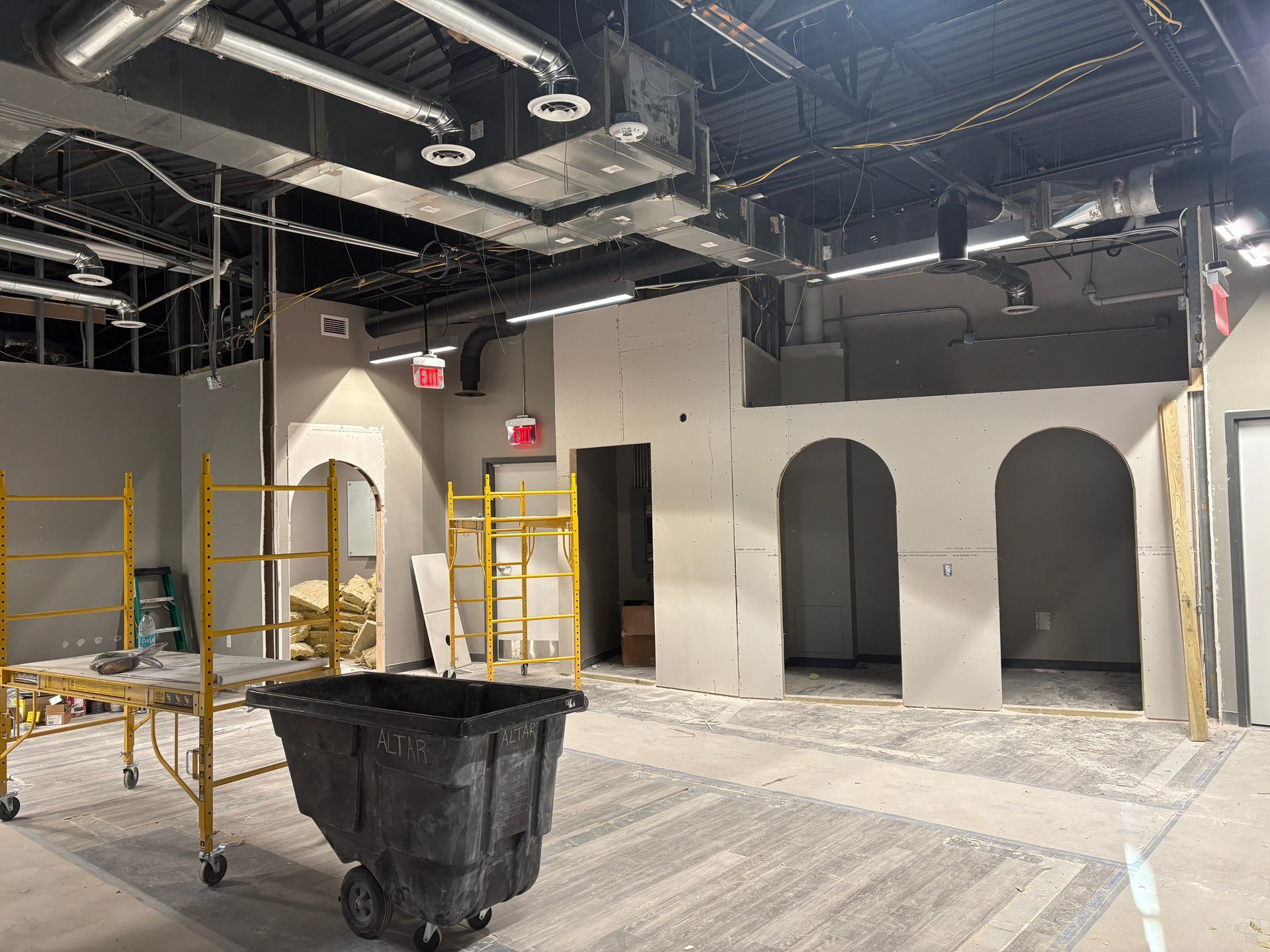 Construction site interior: drywall walls with arched openings, scaffolding, and a trash bin.