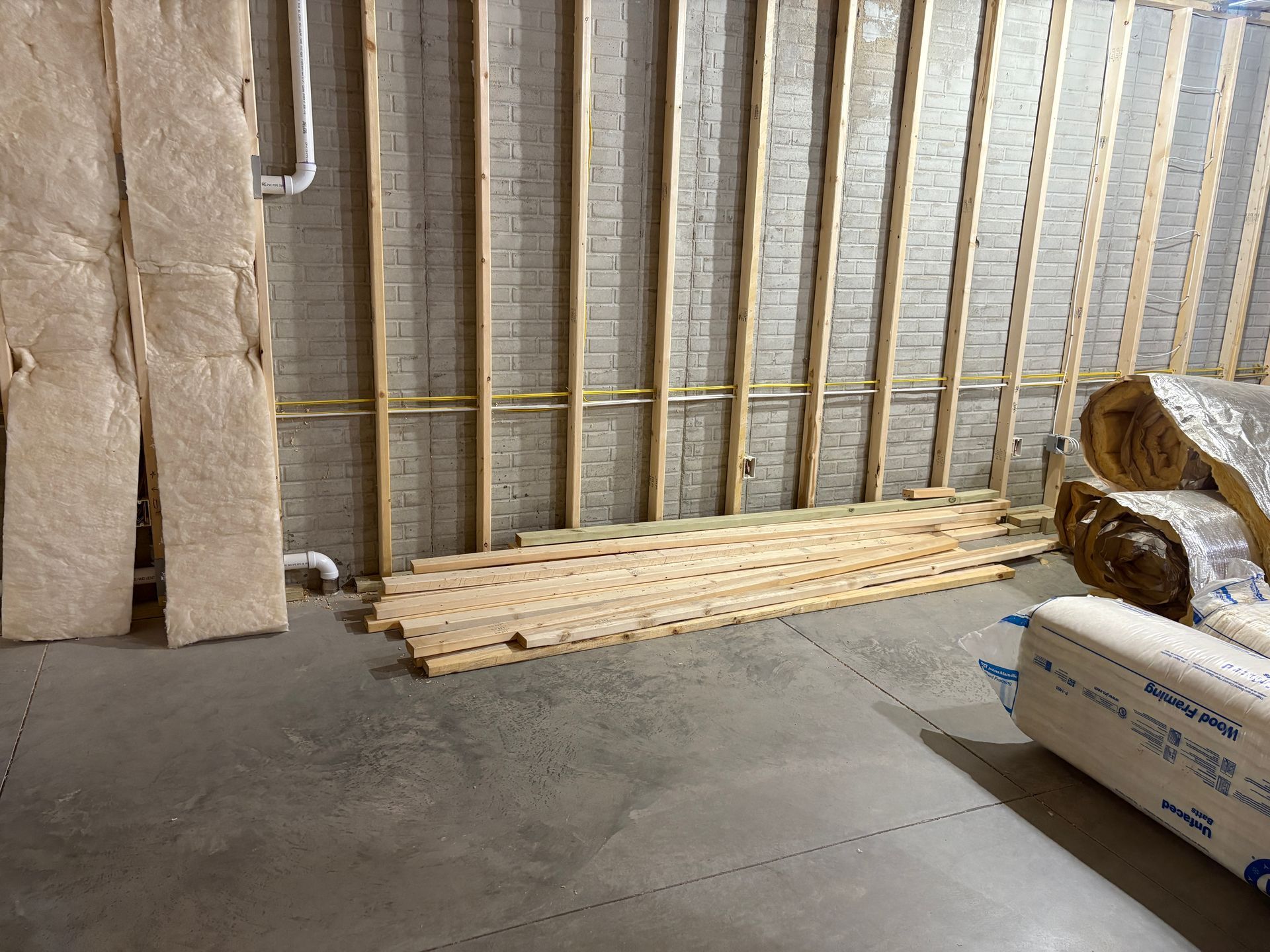 Basement with wooden studs, insulation, and lumber on the floor; construction in progress.