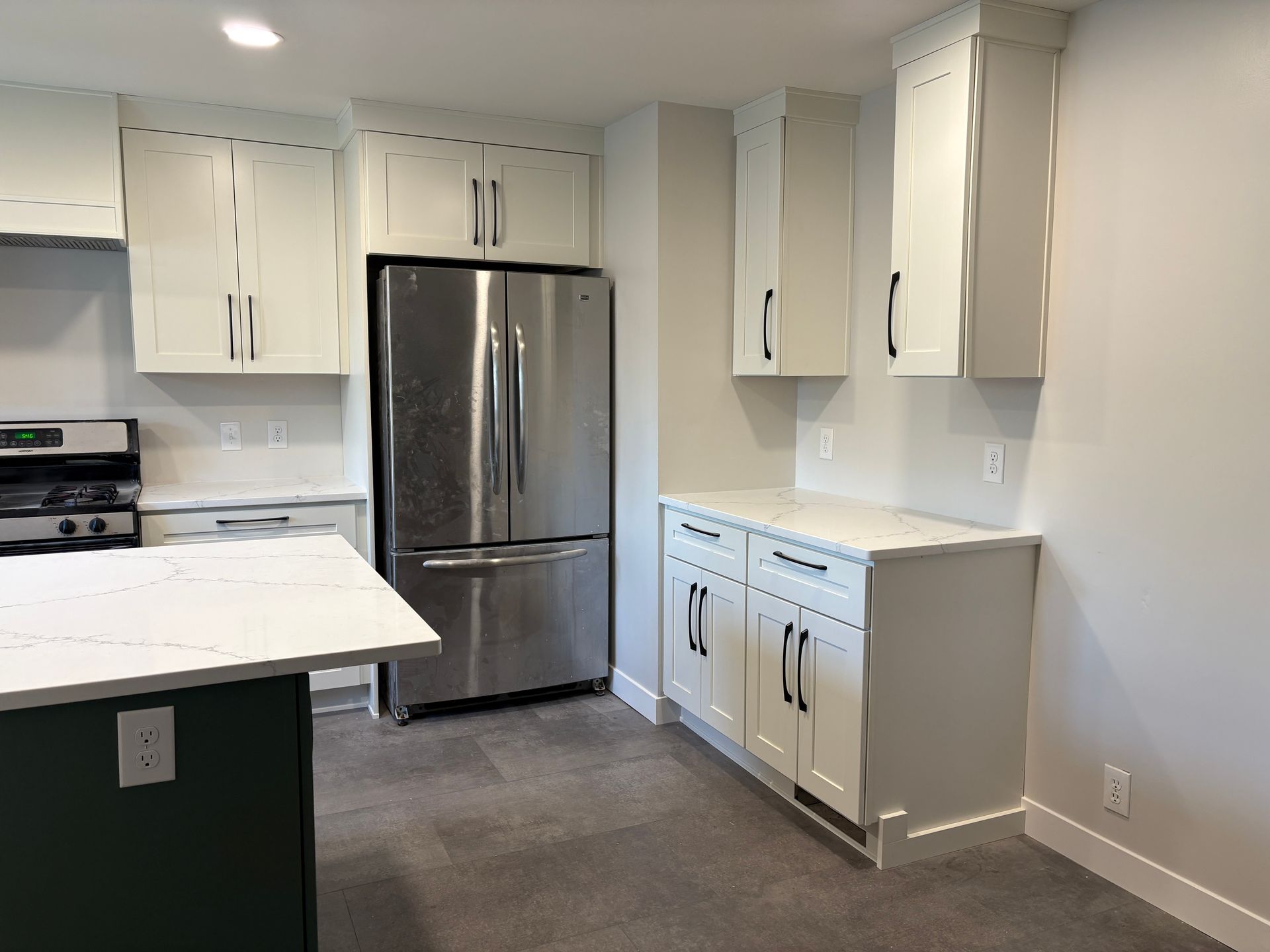 A kitchen with white cabinets, stainless steel refrigerator, and a green island with a white countertop.