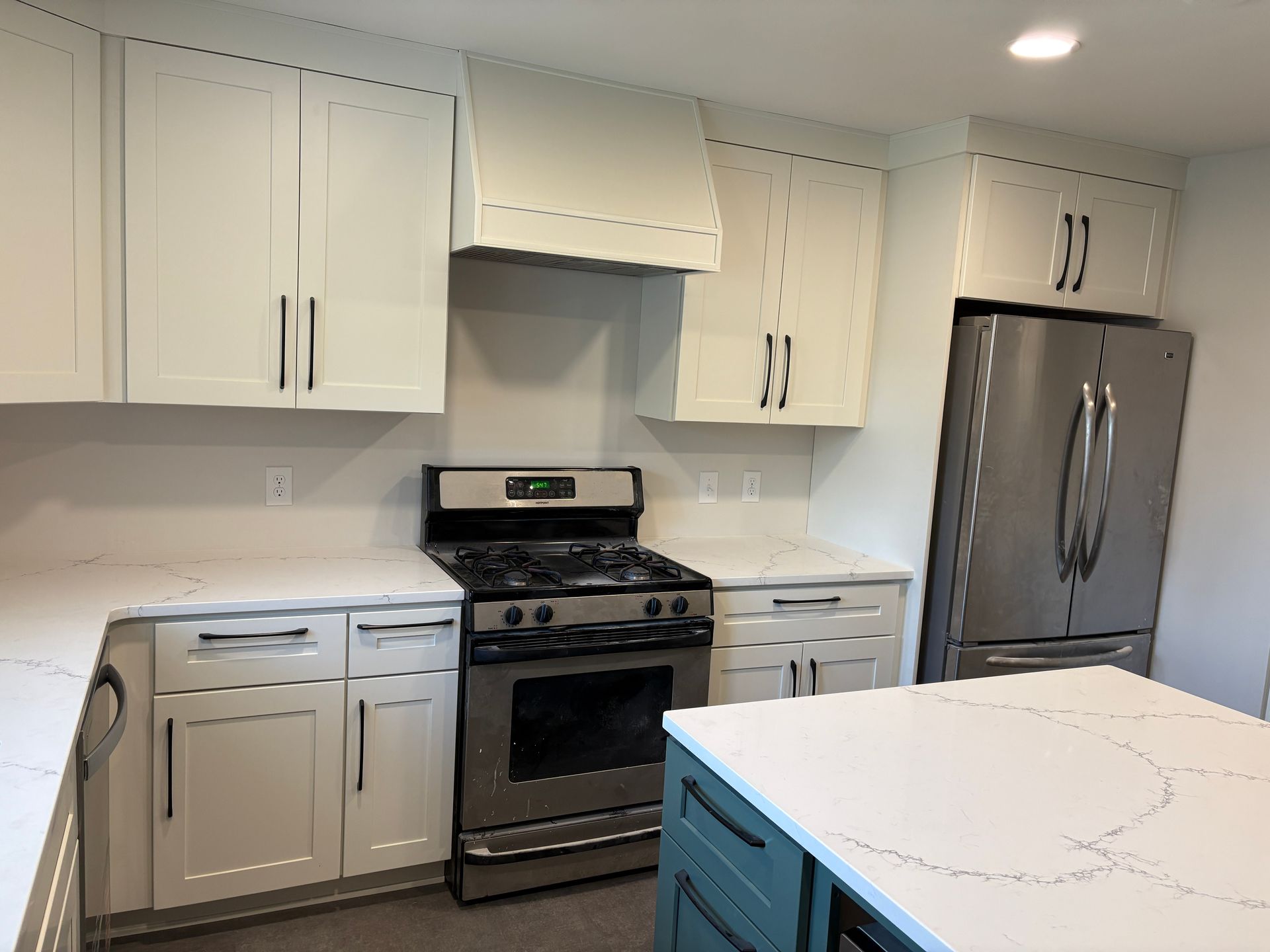 White kitchen with stainless steel appliances, including a refrigerator, range, and a teal island.