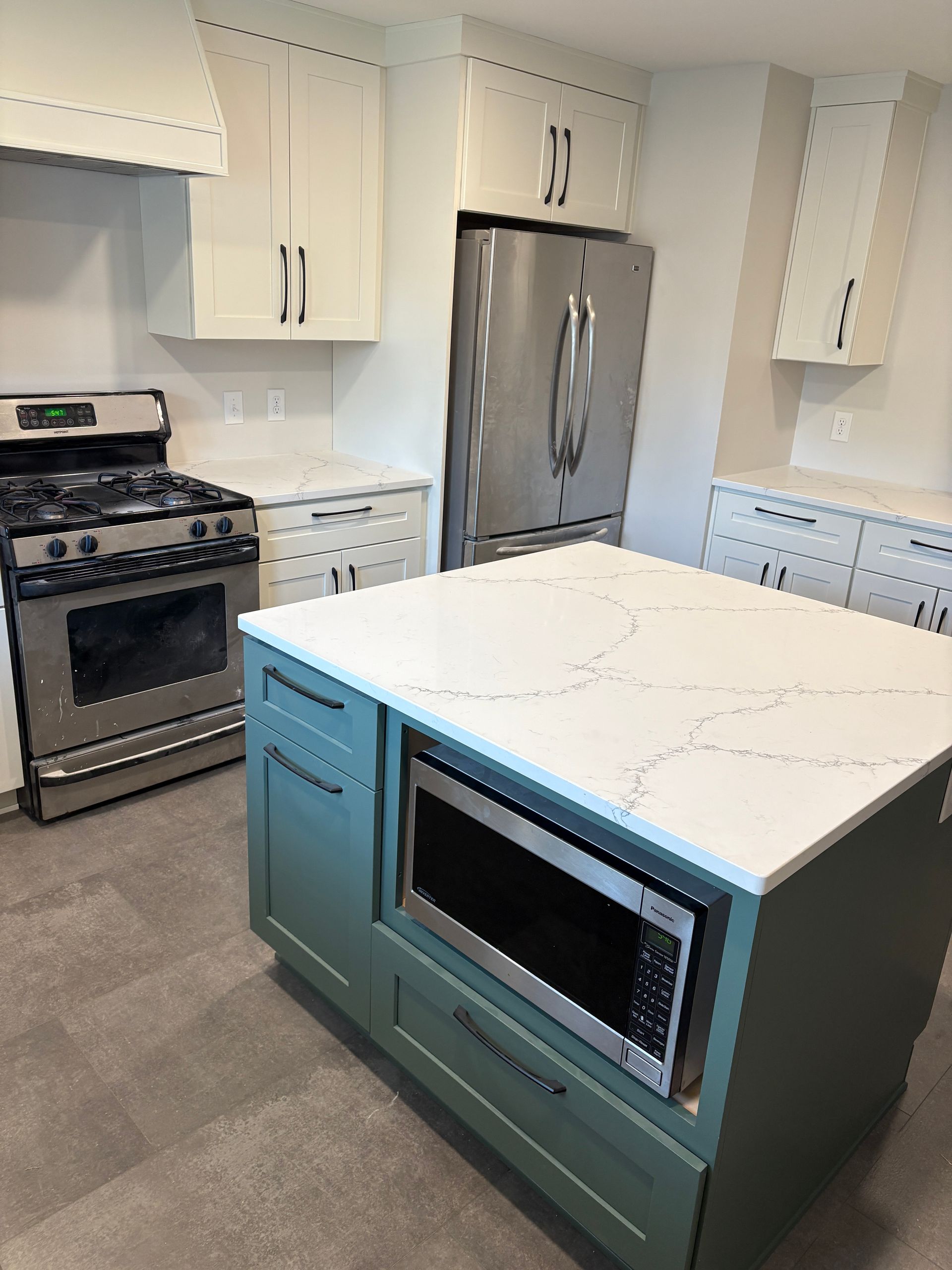 Modern kitchen with stainless steel appliances, white cabinets, and a teal island with a microwave.
