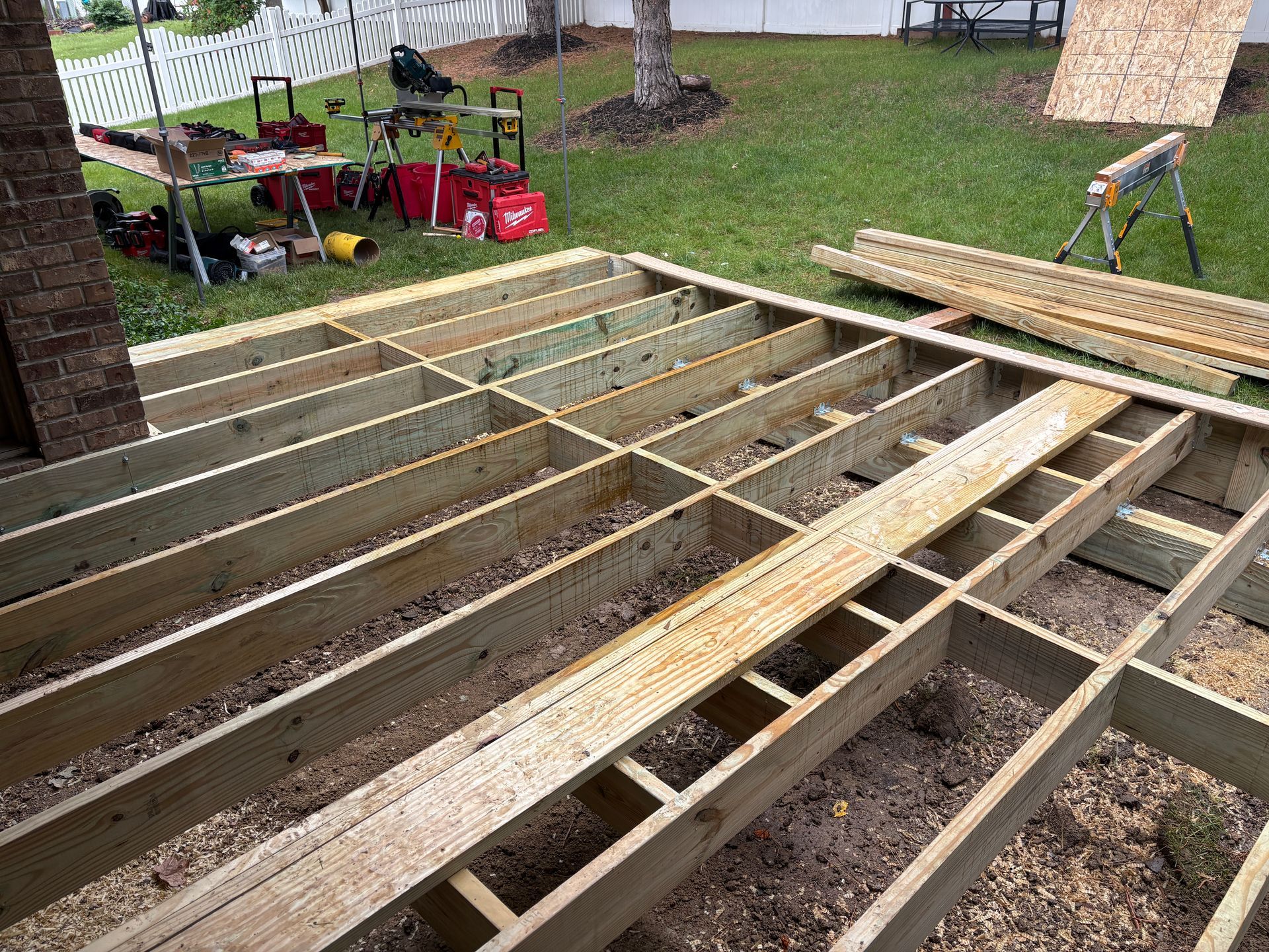 Deck frame under construction on gravel, with tools and lumber nearby.