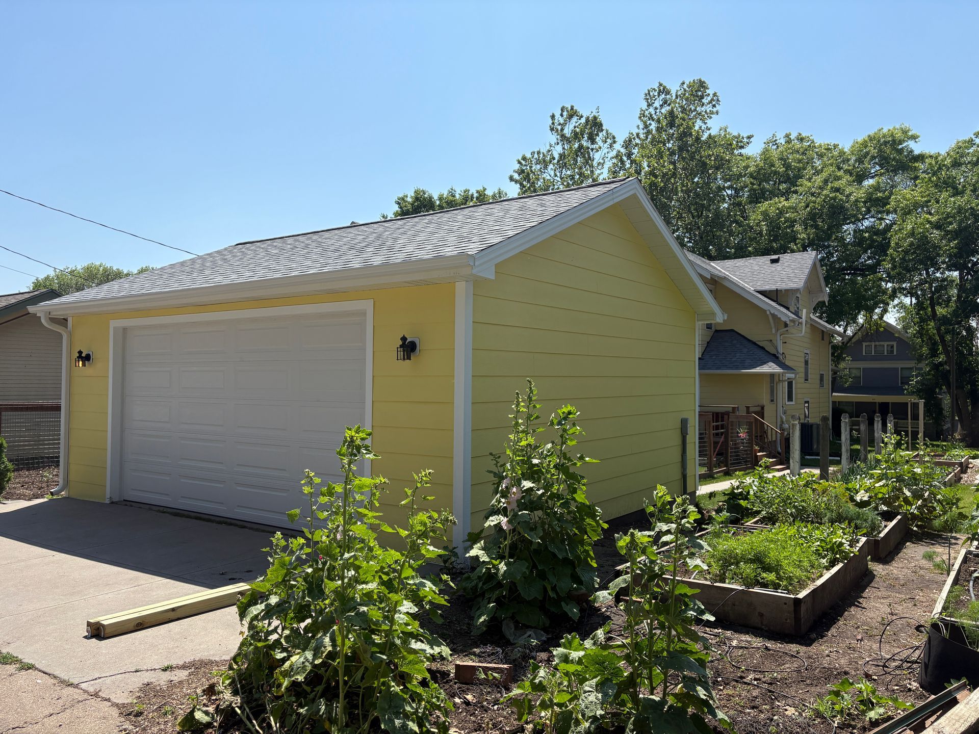 Yellow garage next to a house and garden under a blue sky.