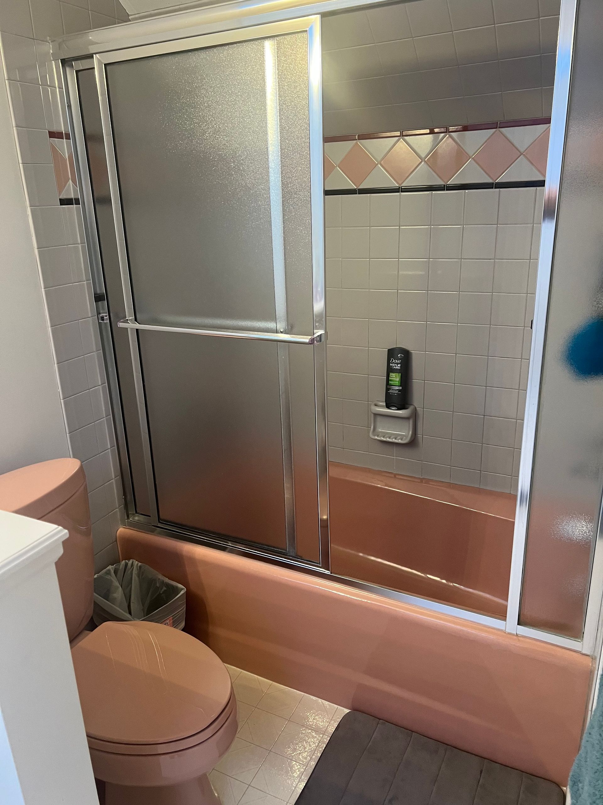 A bathroom with a pink bathtub , toilet , and shower stall.