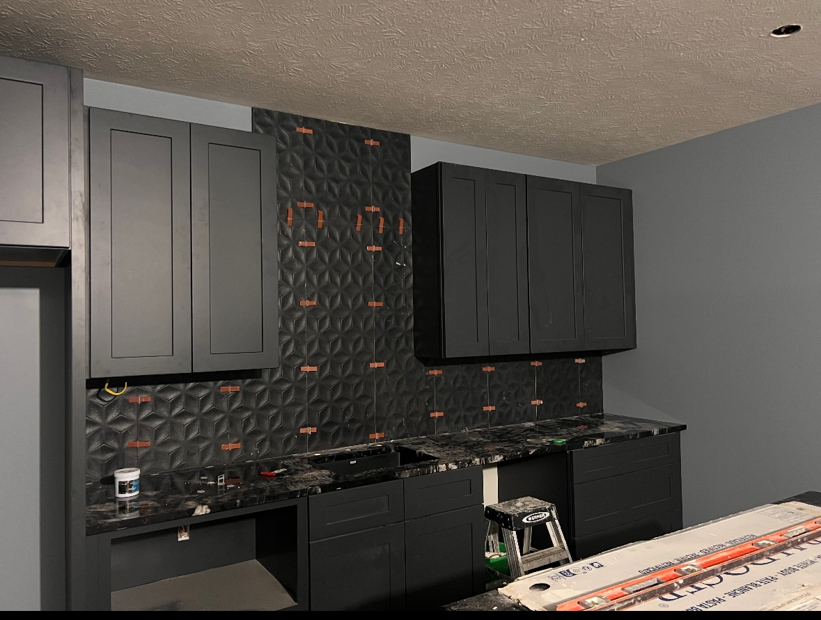 Kitchen with black cabinets, textured backsplash, and countertops.