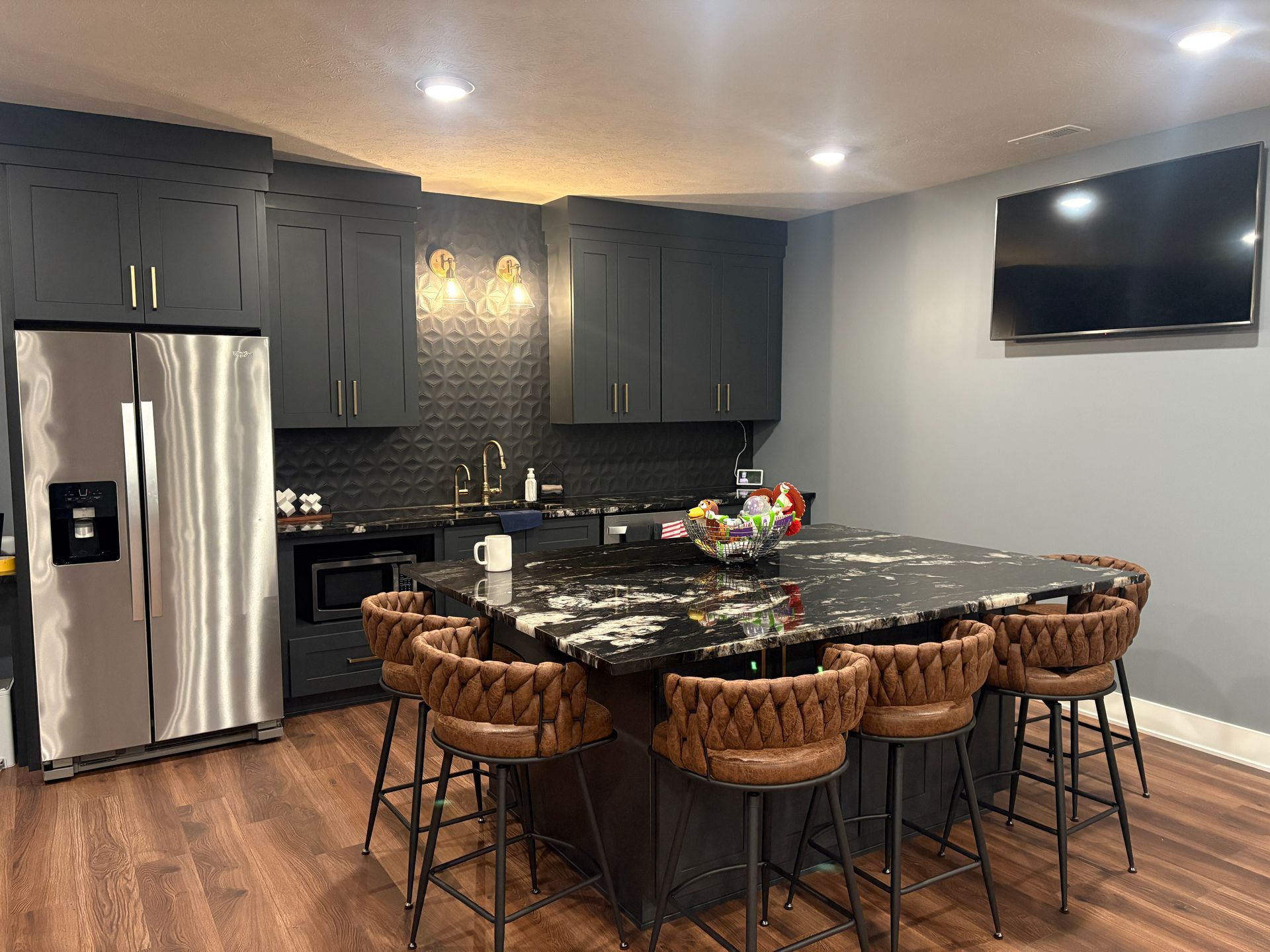 Modern kitchen with dark cabinets, black countertops, a granite island, and brown leather bar stools.
