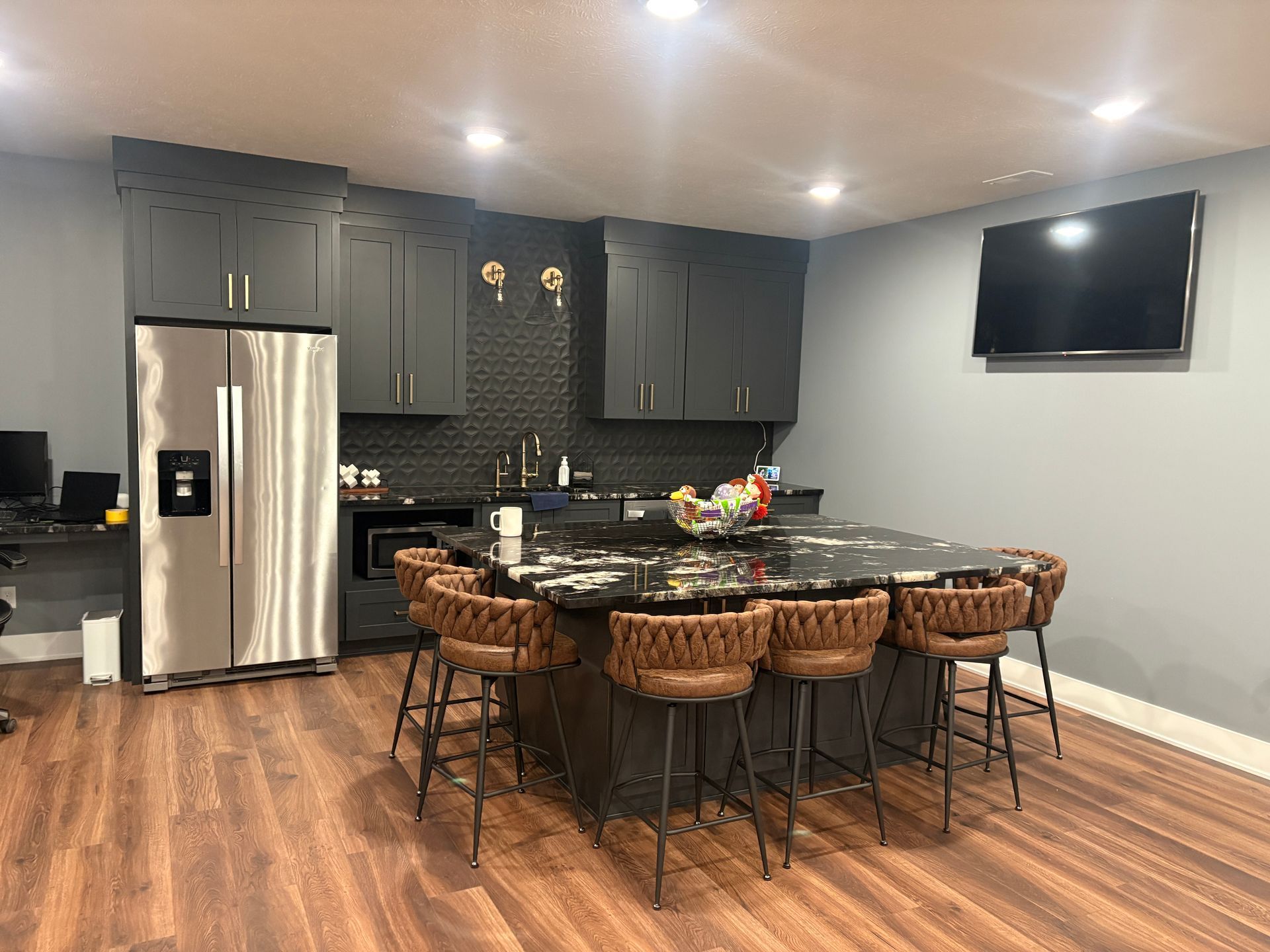 Modern kitchen with island seating, dark cabinets, stainless steel fridge, and mounted TV.
