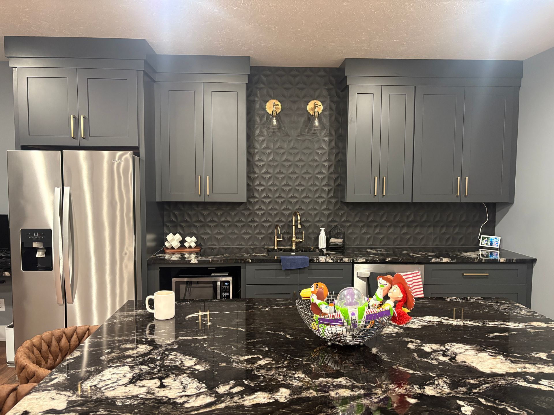 Kitchen with gray cabinets, black countertops, stainless steel appliances, and a dark granite island.