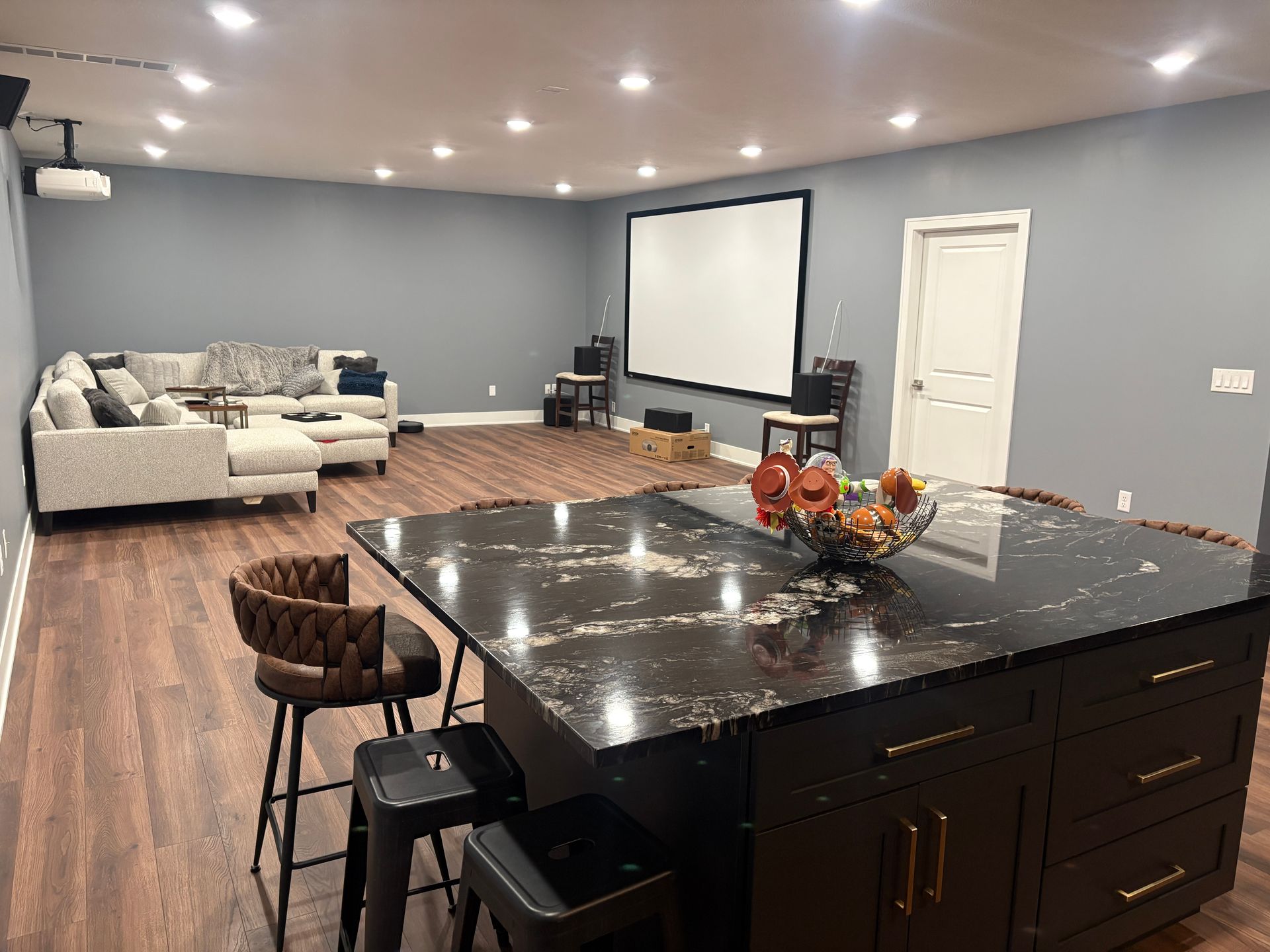 A finished basement with a kitchen island, seating area with a projector screen, and a couch.