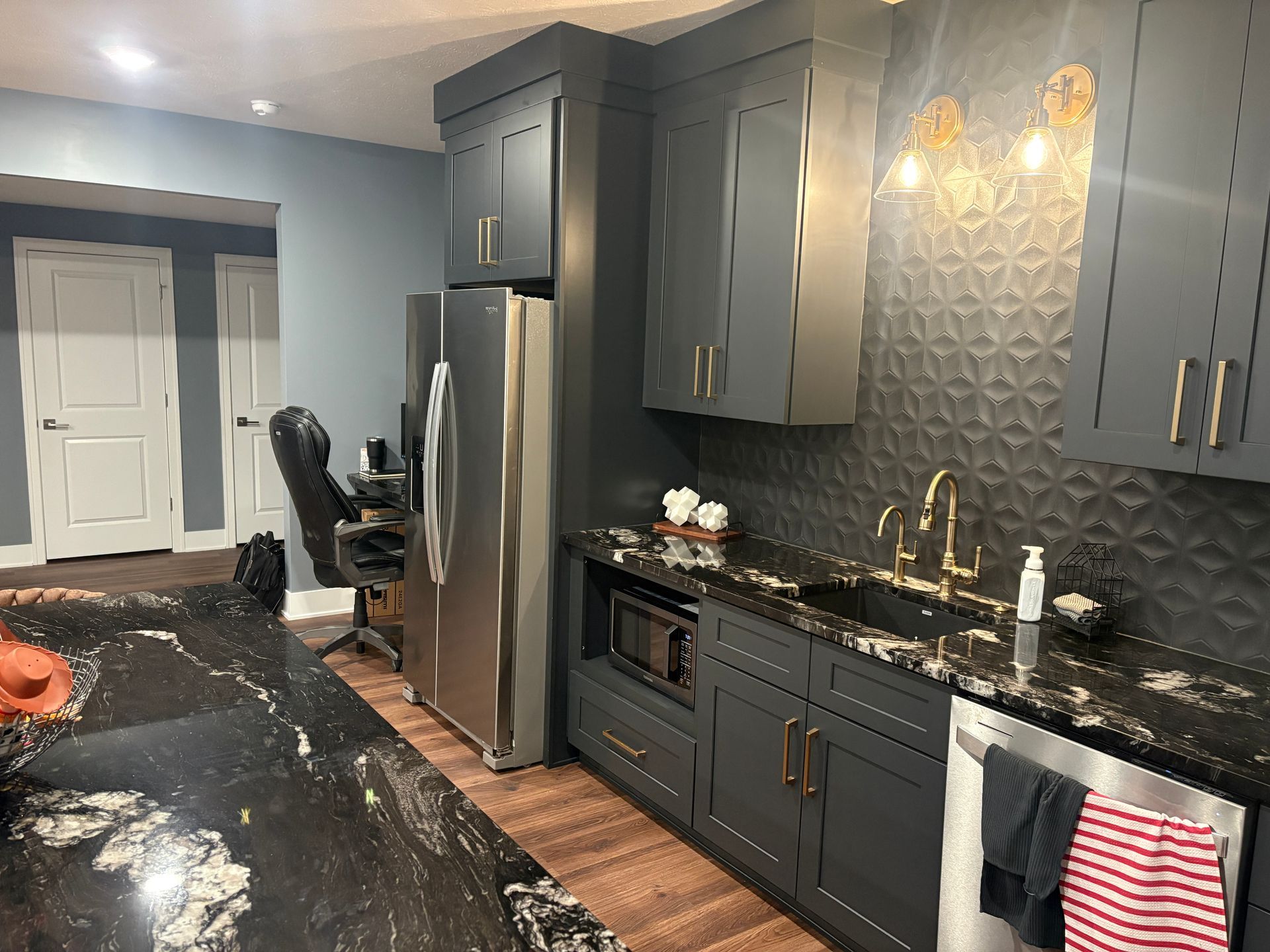 Dark gray kitchen with black countertops, stainless steel appliances, and gold fixtures.