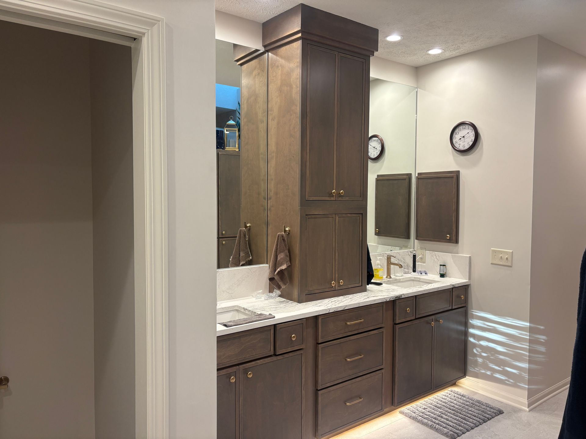 Bathroom with double vanity, tall storage cabinet, and two small mirrors. Brown cabinets, white countertop.