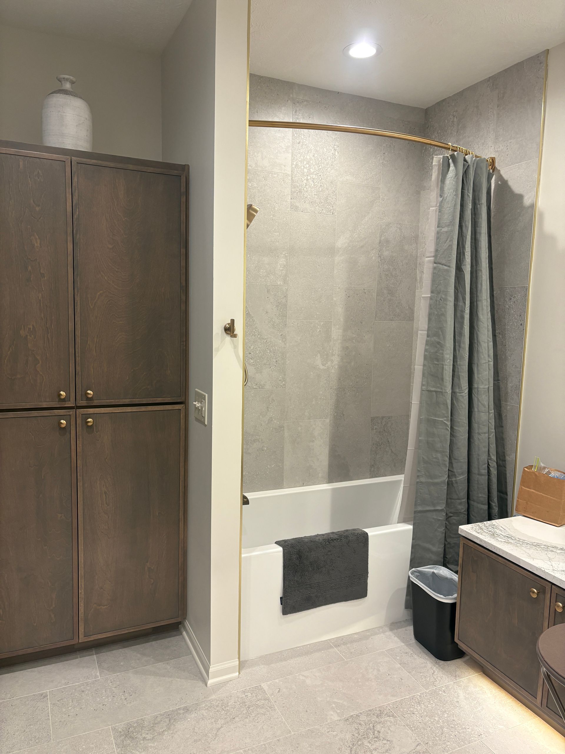 Bathroom with large brown cabinets, a gray tiled shower, and a white bathtub.
