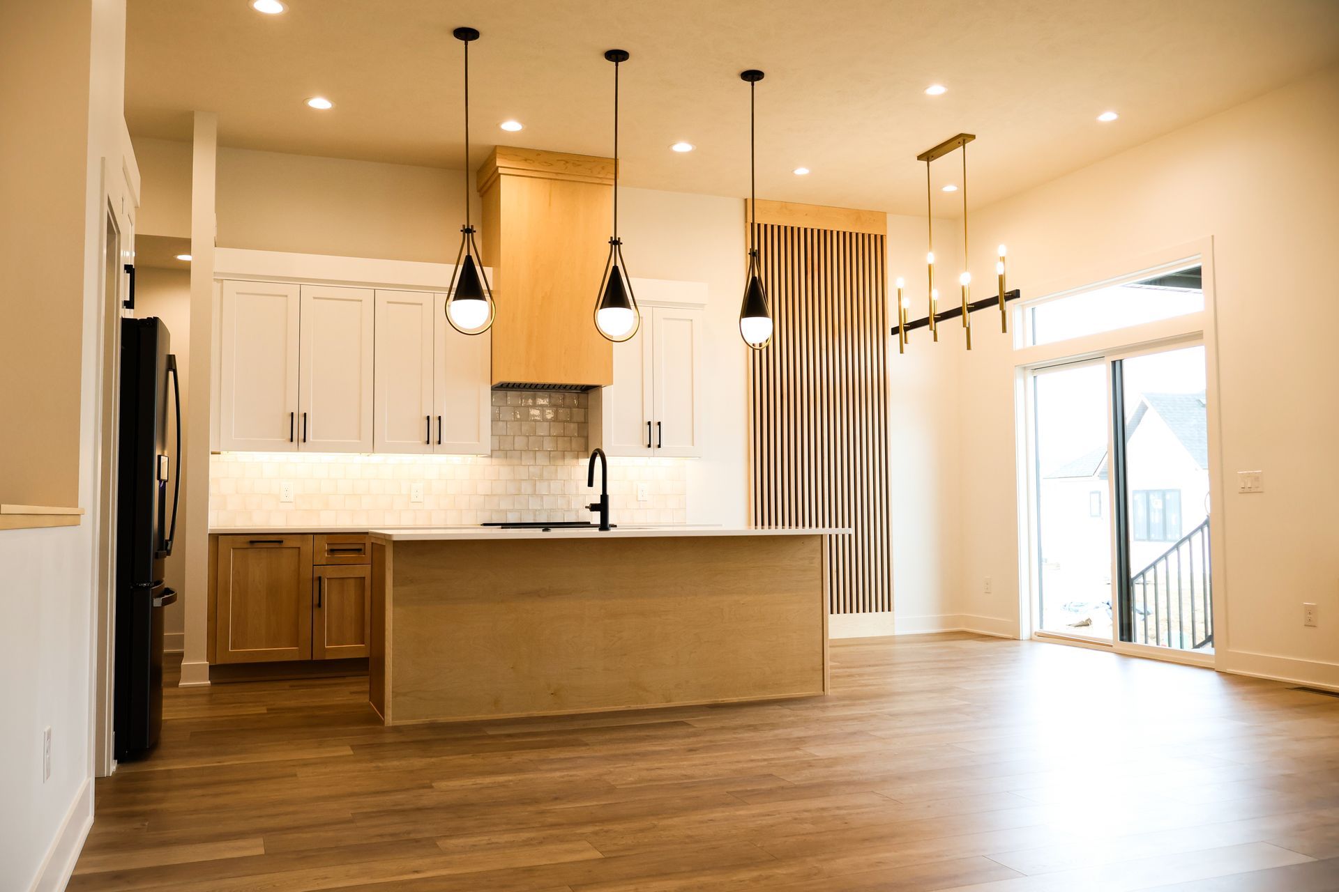 Modern kitchen with light wood floors, cabinets, island, and hanging pendant lights.