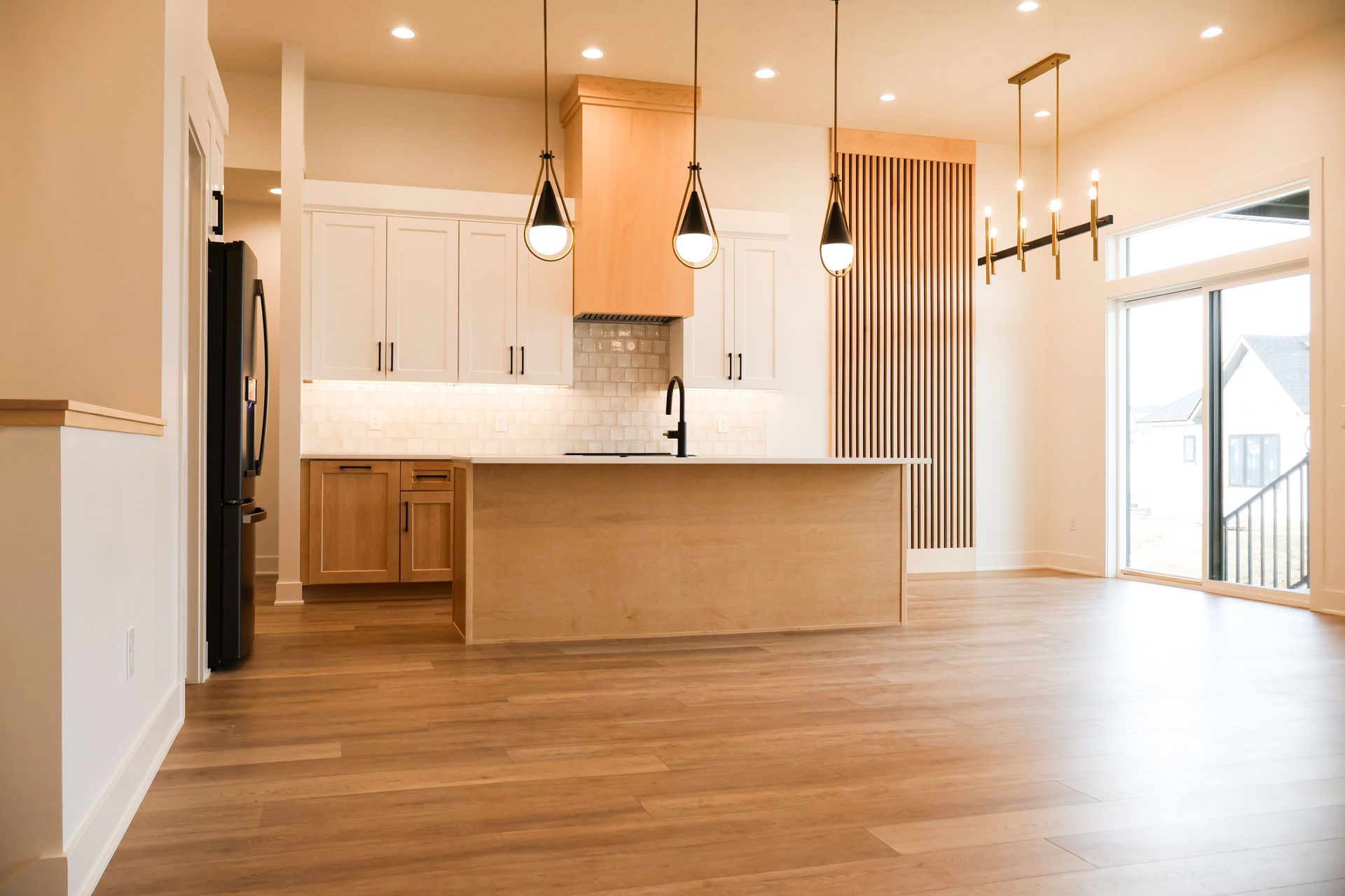Spacious kitchen with wood floors, light cabinets, island, black appliances, and large windows.