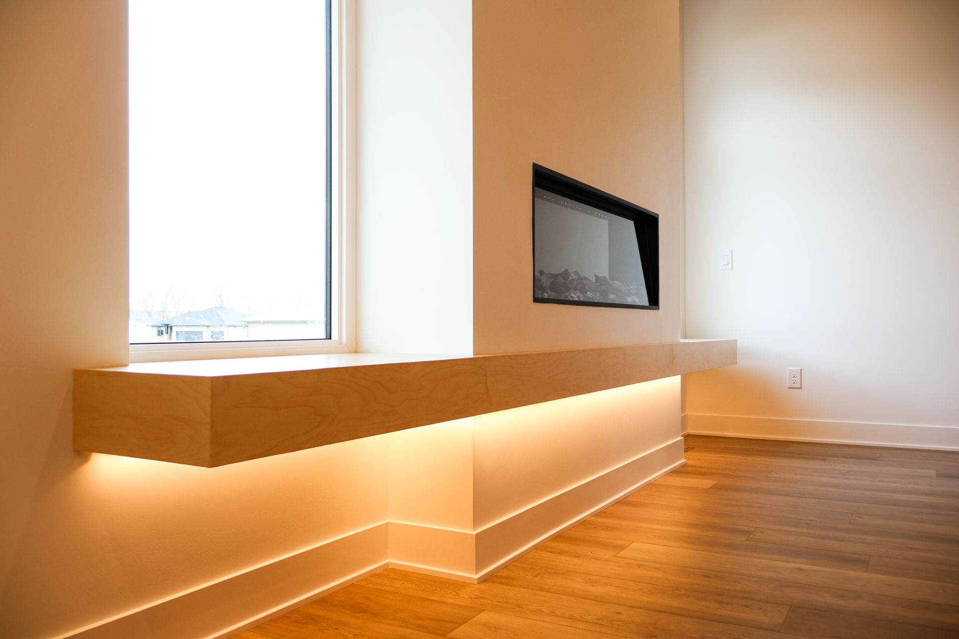 Modern room with wooden shelf and baseboard illuminated by warm lights, electric fireplace, and window.