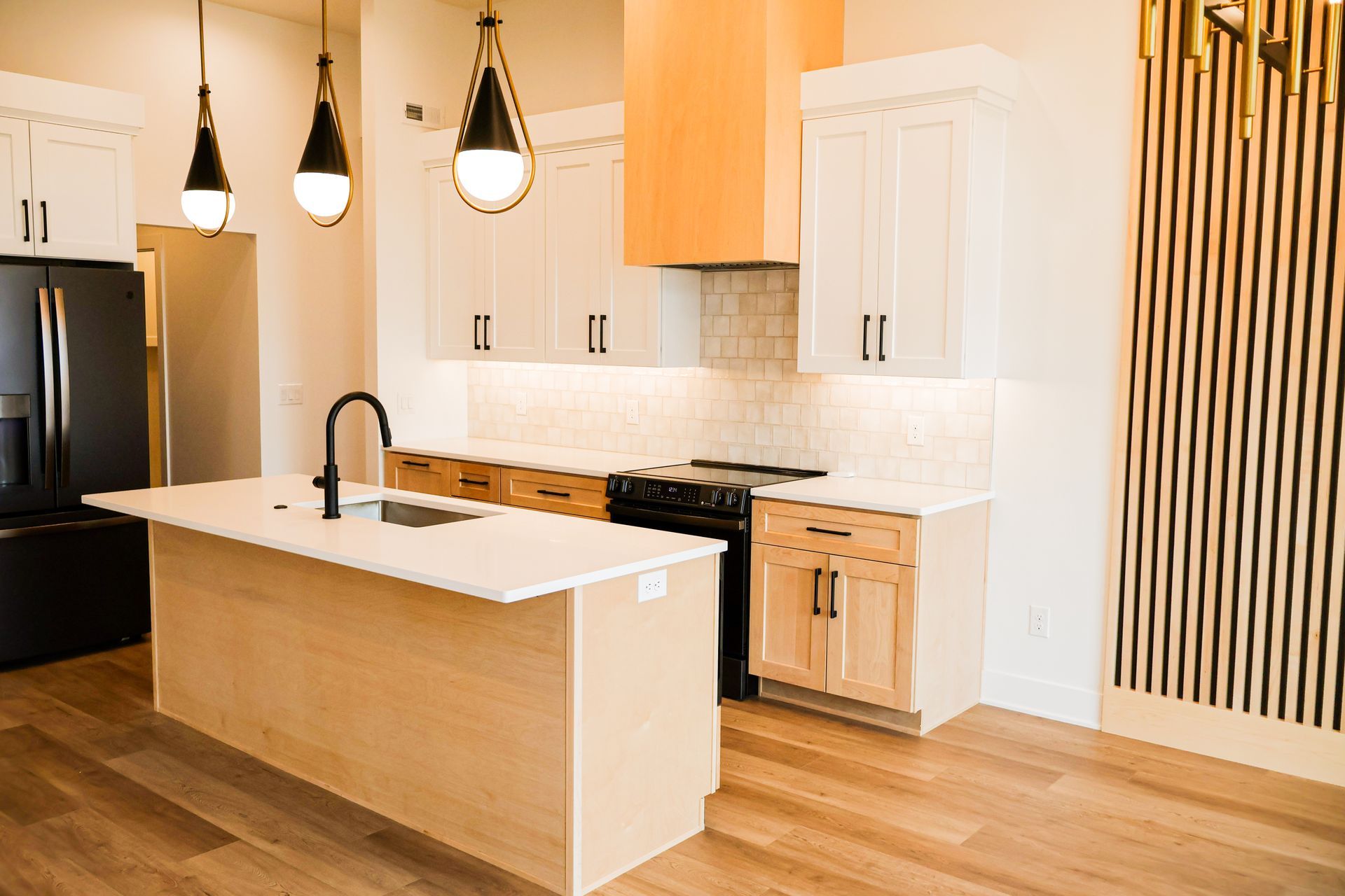 Modern kitchen with island, white and wood cabinets, black appliances, and pendant lights.