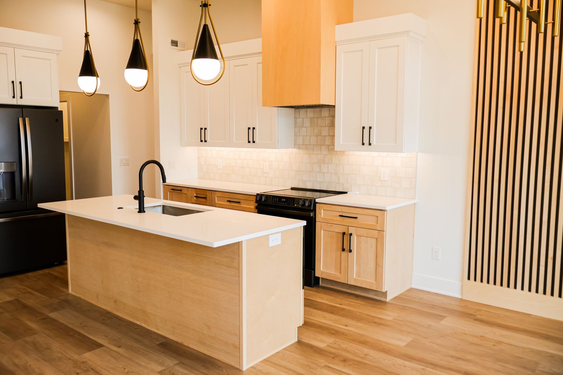 Modern kitchen with white and wood cabinets, black appliances, and pendant lights.