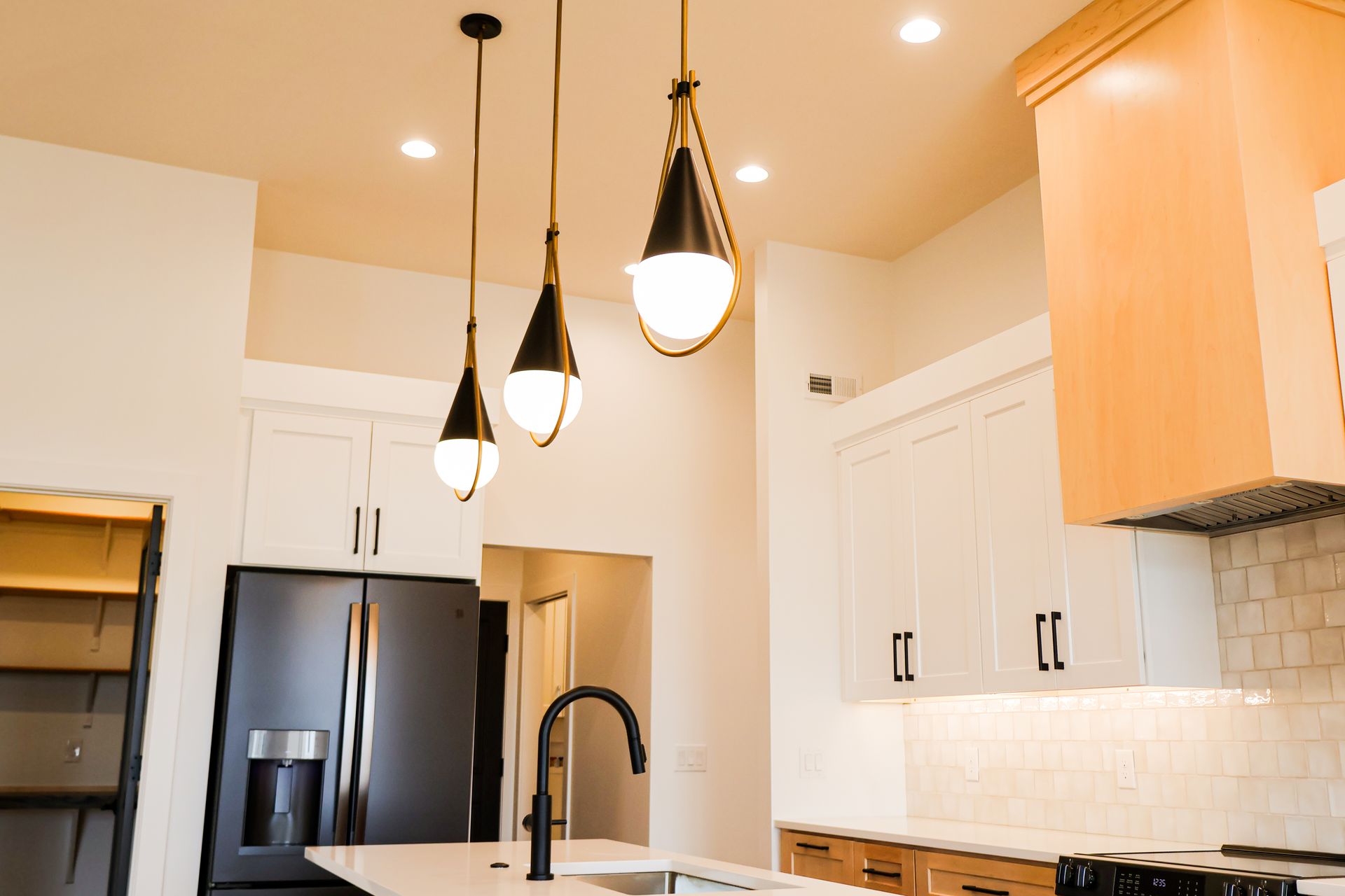 Modern kitchen with pendant lights, black appliances, white cabinets, and island with a sink.
