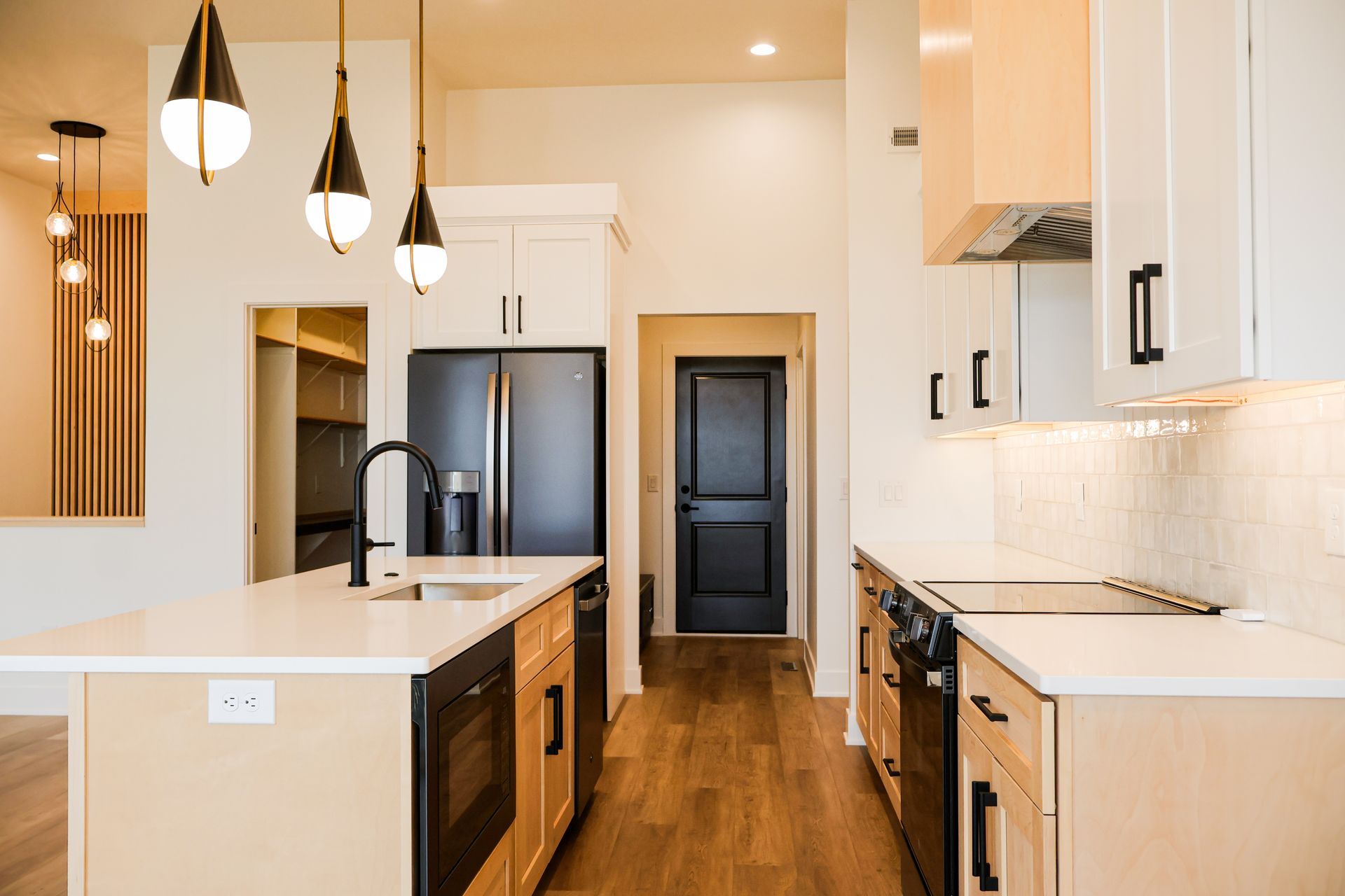 Modern kitchen with island, white countertops, black appliances, and pendant lights.