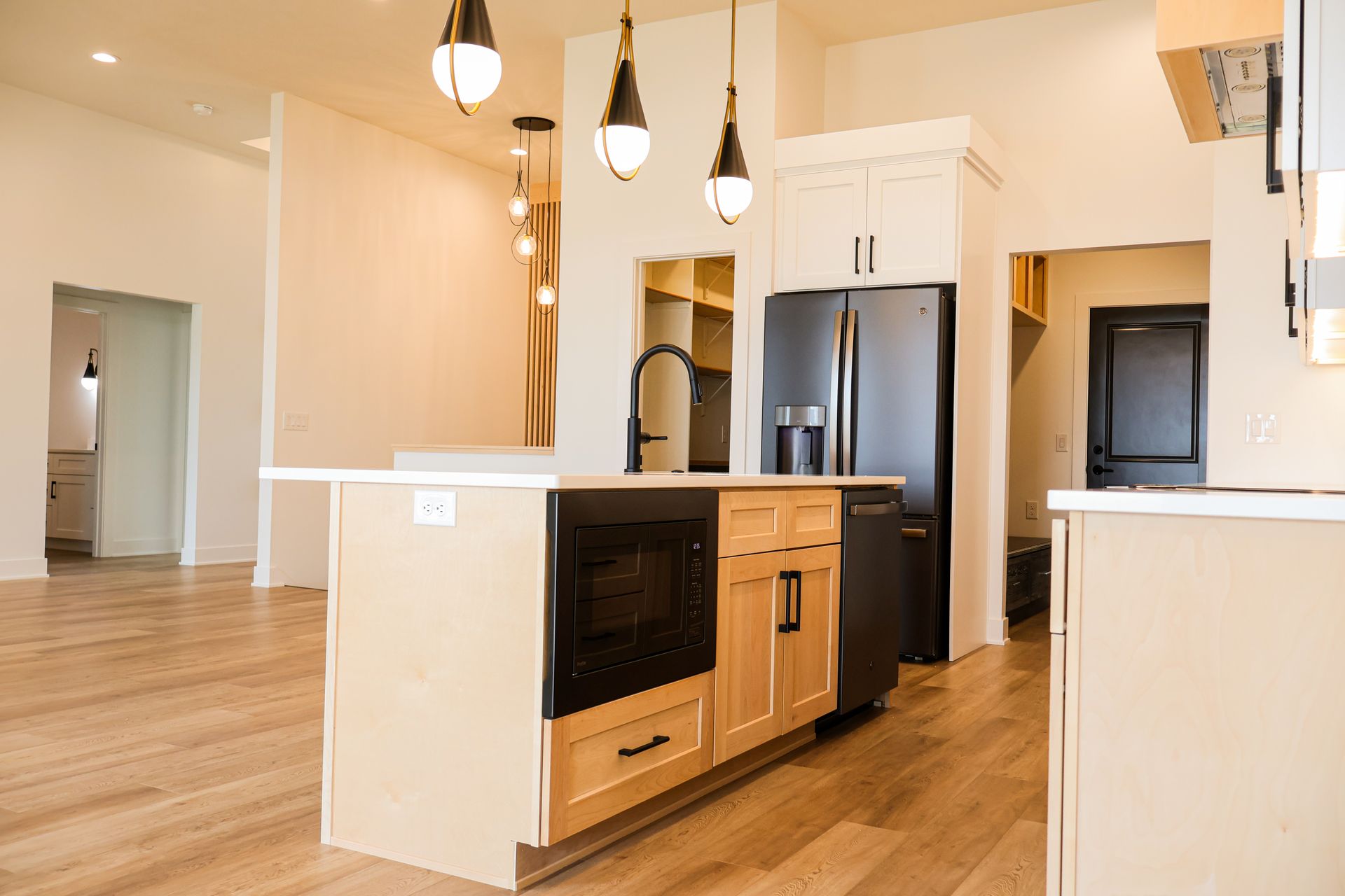 Modern kitchen with island, black appliances, light wood cabinets and floors, pendant lights.